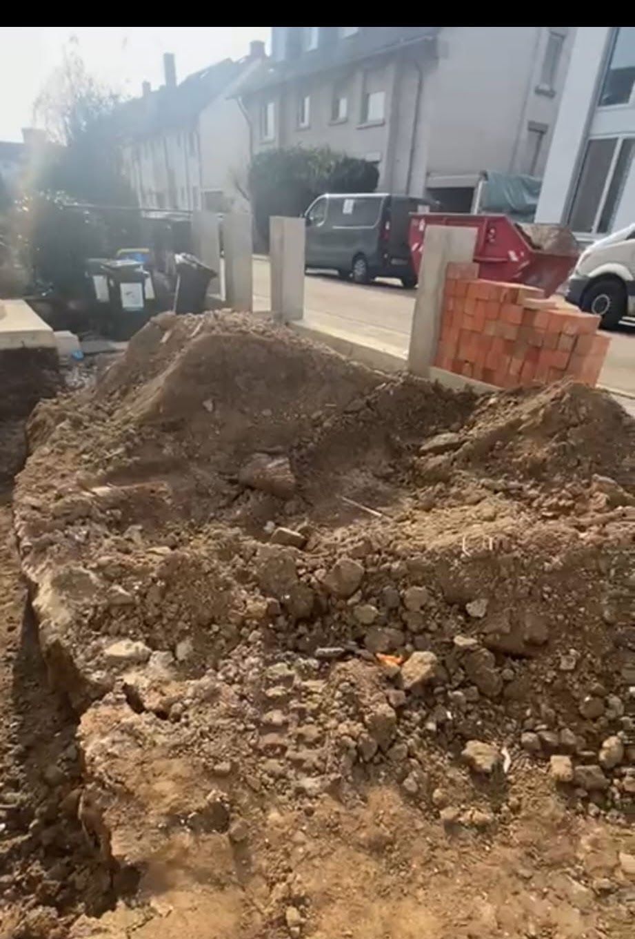 Ein Haufen Erde und Baumaterialien vor einer Wohnstraße. Graue Säulen und Ziegelsteine ​​sind zu sehen.