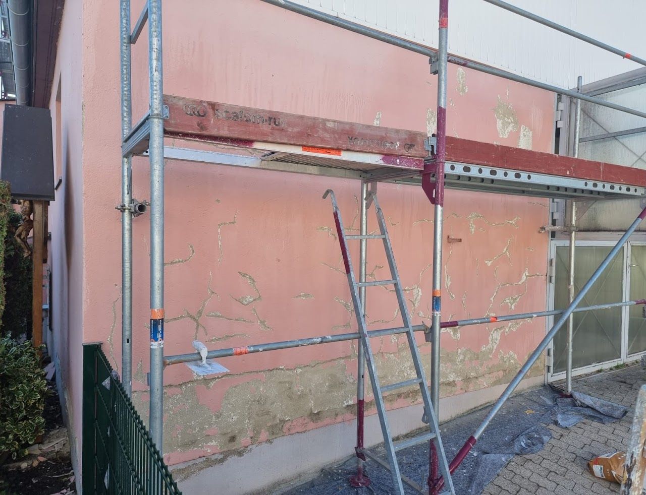 Ein Gerüst steht neben einem pfirsichfarbenen Gebäude mit beschädigtem Putz, das für die Renovierung bereit ist.
