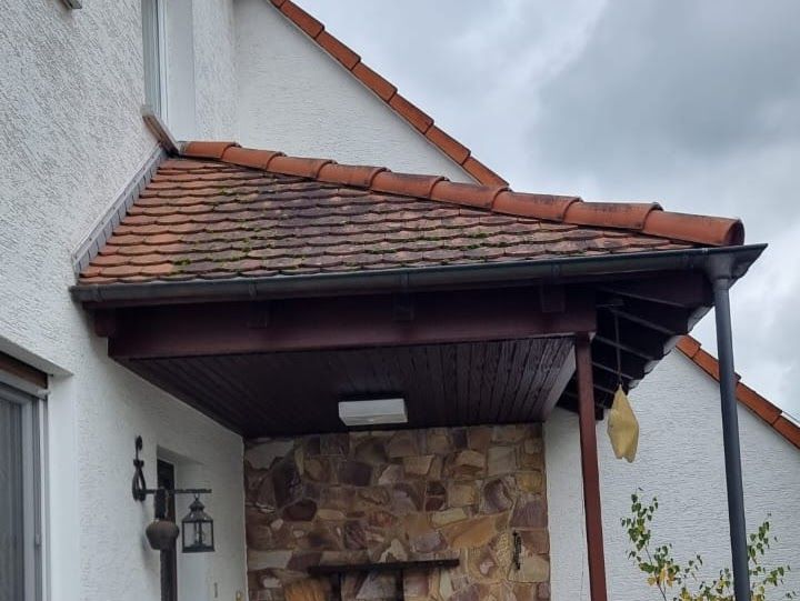 Überdachte Veranda mit rotem Ziegeldach, braunen Holzverkleidungen und Steinmauer.