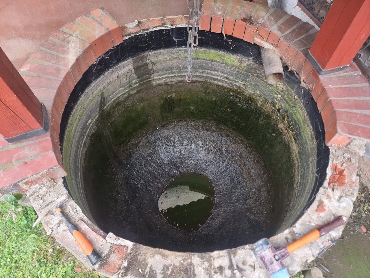 Mit Ziegeln ausgekleideter Brunnen, runde Öffnung, mit Wasser gefüllt, umgeben von roten und weißen Ziegeln, im Freien.