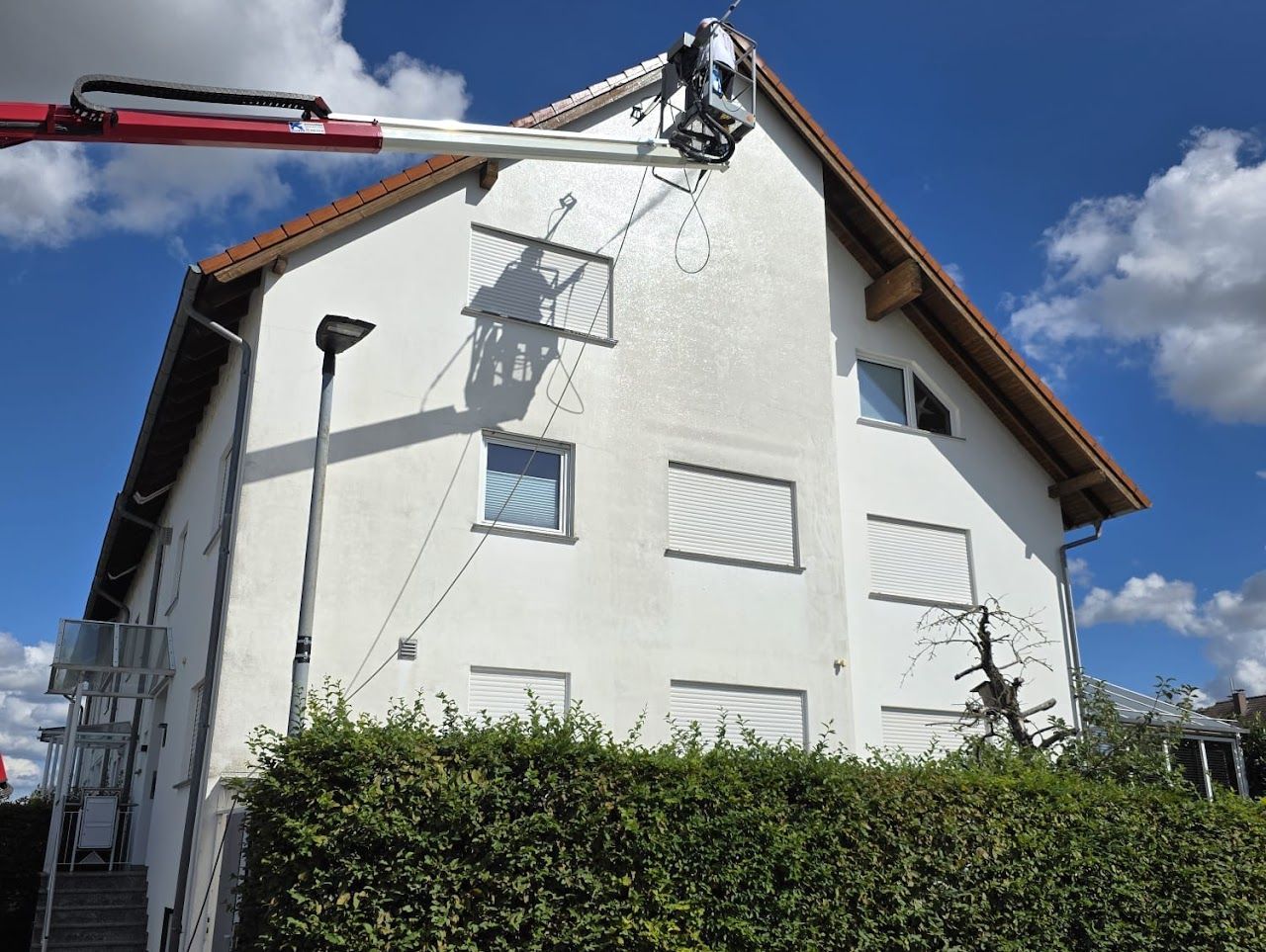 Ein Gabelstapler arbeitet an einem weißen Gebäude vor blauem Himmel über einer grünen Hecke.