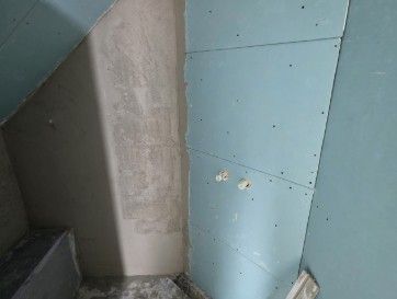 Innenecke mit einer teilweise fertiggestellten Wand aus blauen Gipskartonplatten und grauem Putz.