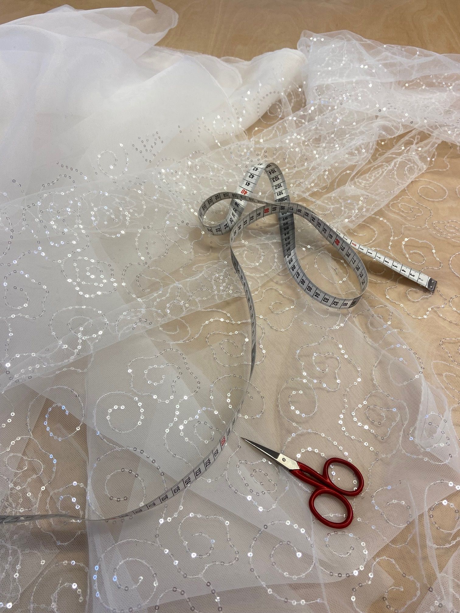 Eine Schere liegt auf einem Stück weißem Stoff neben einem Maßband.