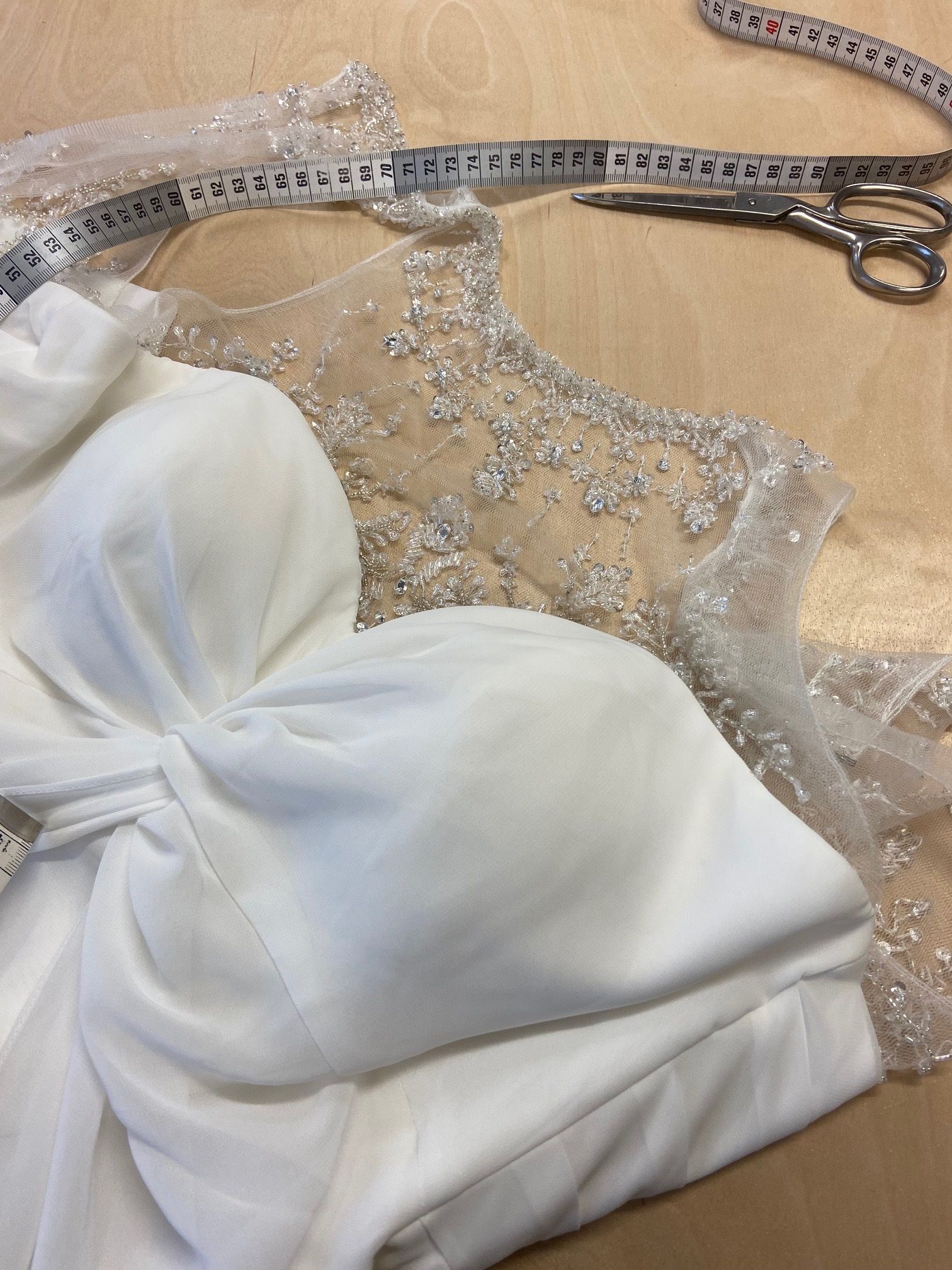 Auf einem Tisch liegt ein weißes Kleid neben einem Maßband und einer Schere.