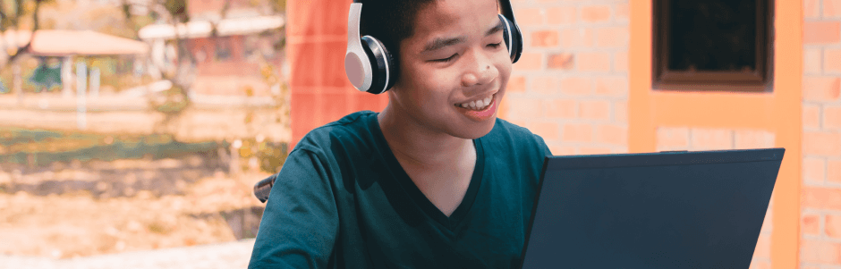 A young boy wearing headphones is using a laptop computer.