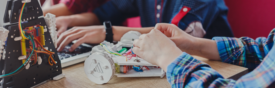 A group of children are sitting at a table making a robot.