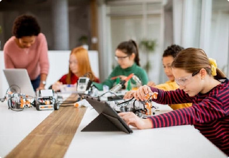 A group of children are sitting at a table working on a robot.