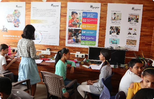 A group of people are sitting at desks in a room with posters on the wall.