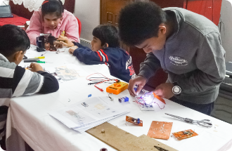 A group of children are sitting at a table working on electronics