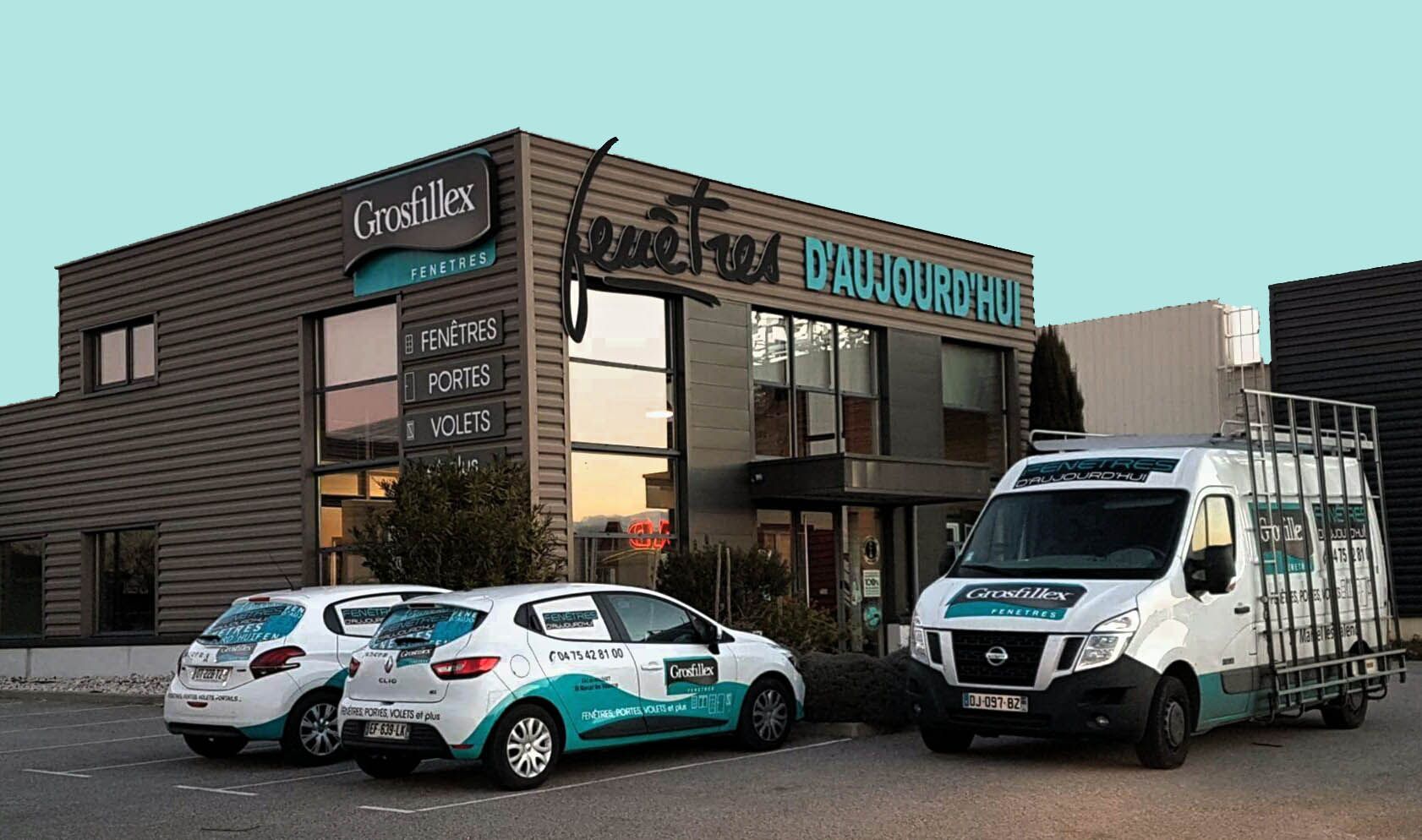 Un bâtiment commercial, avec deux voitures de marque et une camionnette de travail garées devant.