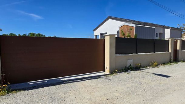 Portail coulissant et clôture avec une maison en arrière-plan.