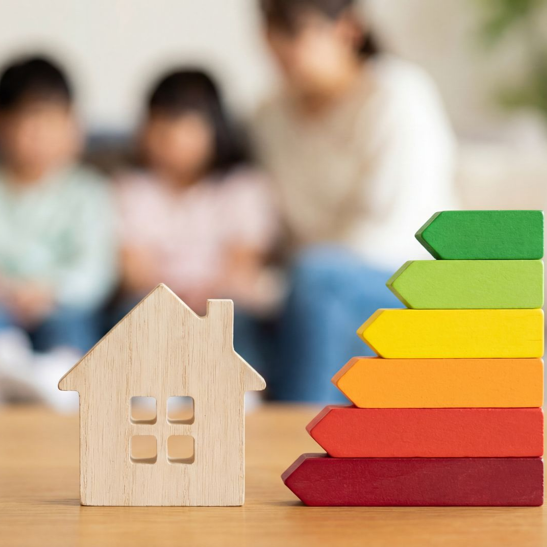 Une maquette de maison en bois à côté d'un escalier coloré représentant une cote d'efficacité énergétique.