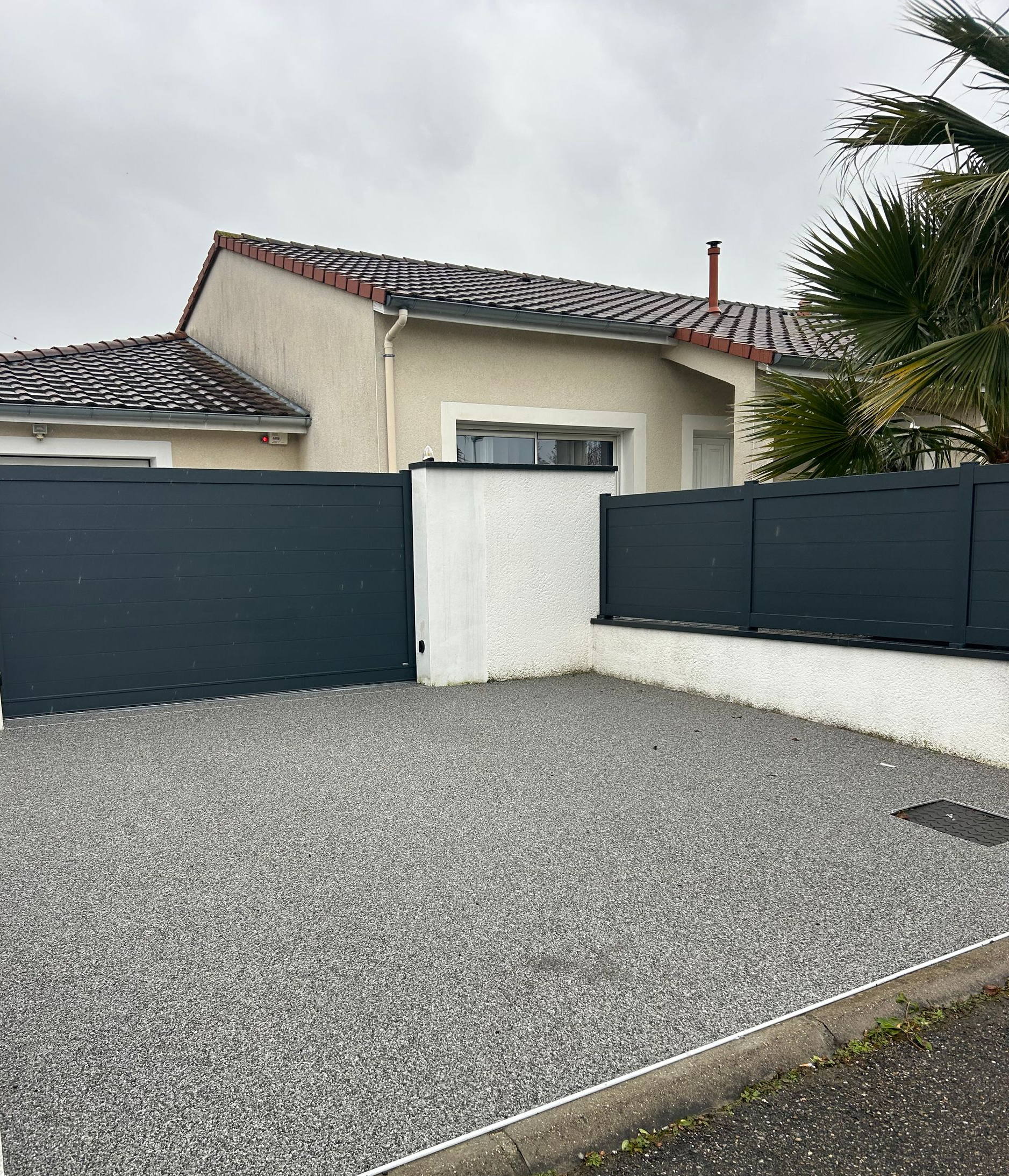 L'extérieur d'une maison résidentielle avec une allée en gravier gris, un muret blanc et des panneaux d'intimité horizontaux gris foncé.