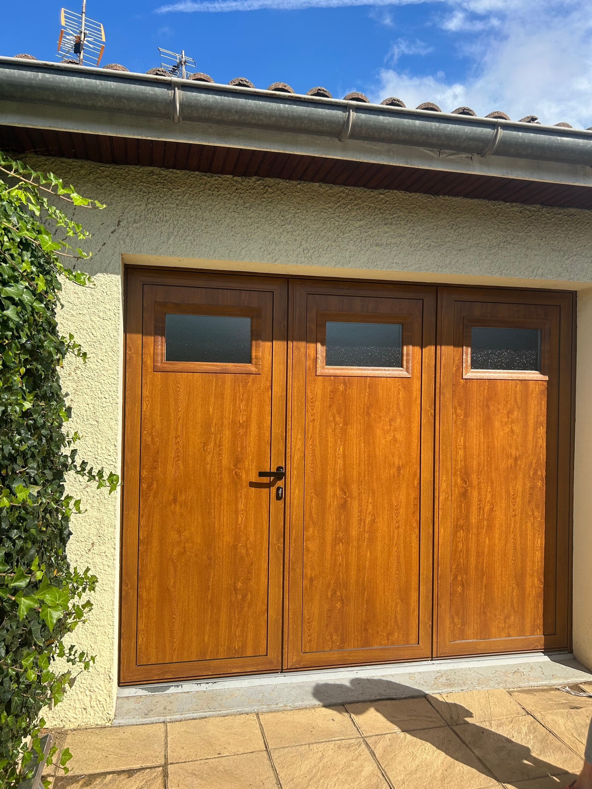 Portes de garage doubles en bois avec petites fenêtres sur une maison en stuc sous un ciel bleu.