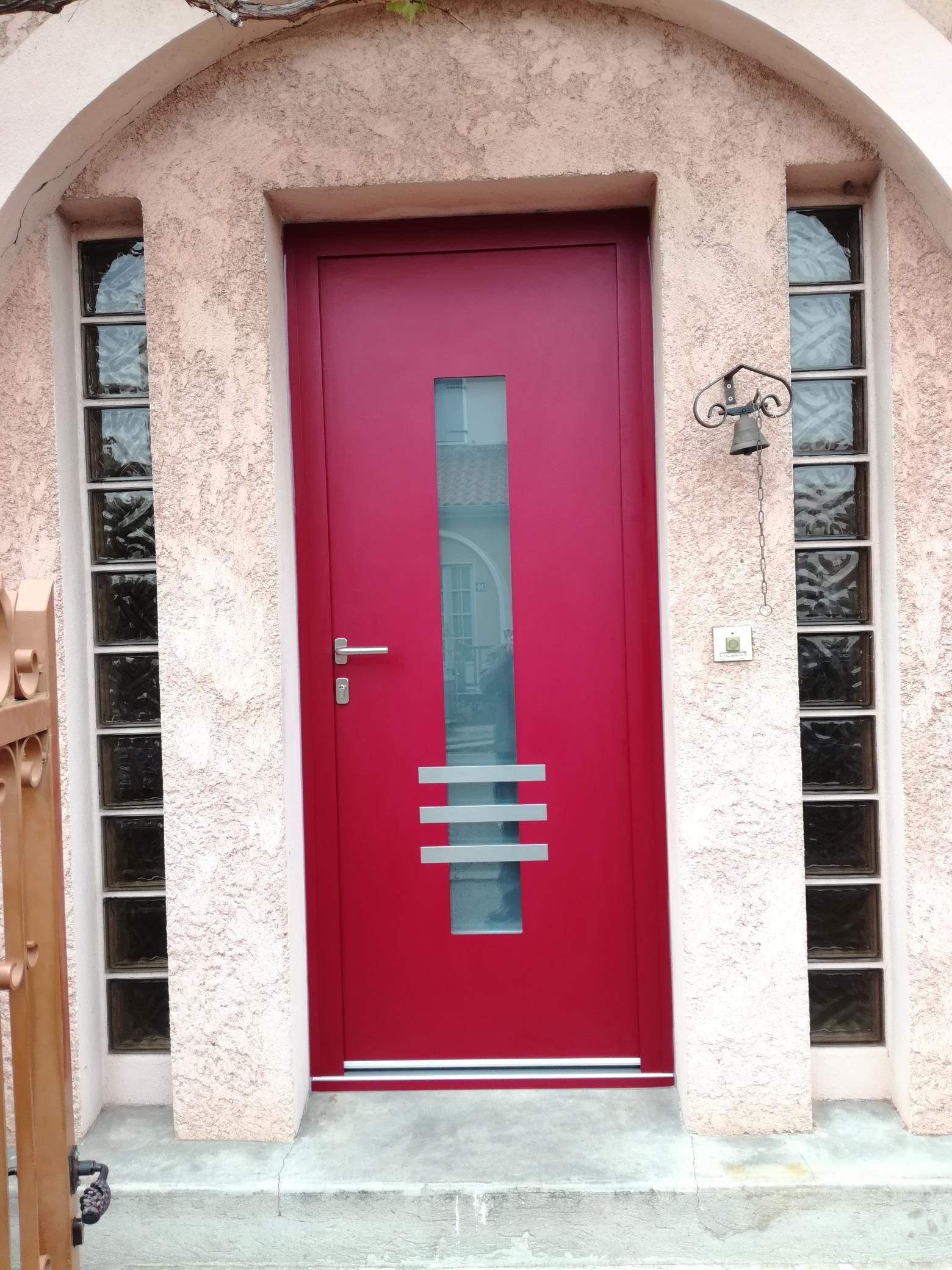 Une porte d'entrée rouge moderne avec une vitre verticale et des rayures horizontales dépolies, encadrée par des fenêtres verticales en pavés de verre.