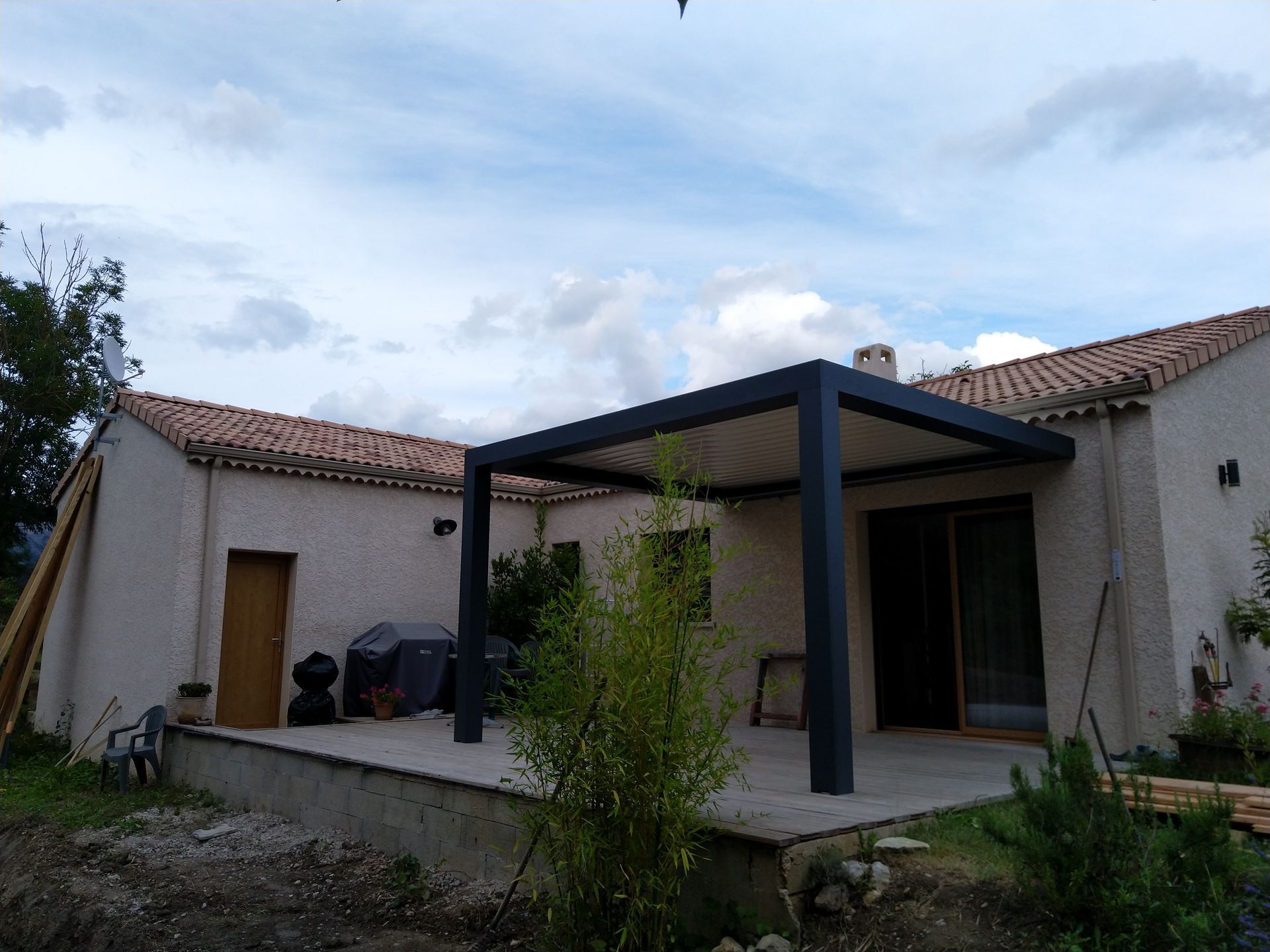L'extérieur beige de cette maison présente un patio avec une grande pergola noire moderne sous un ciel nuageux.