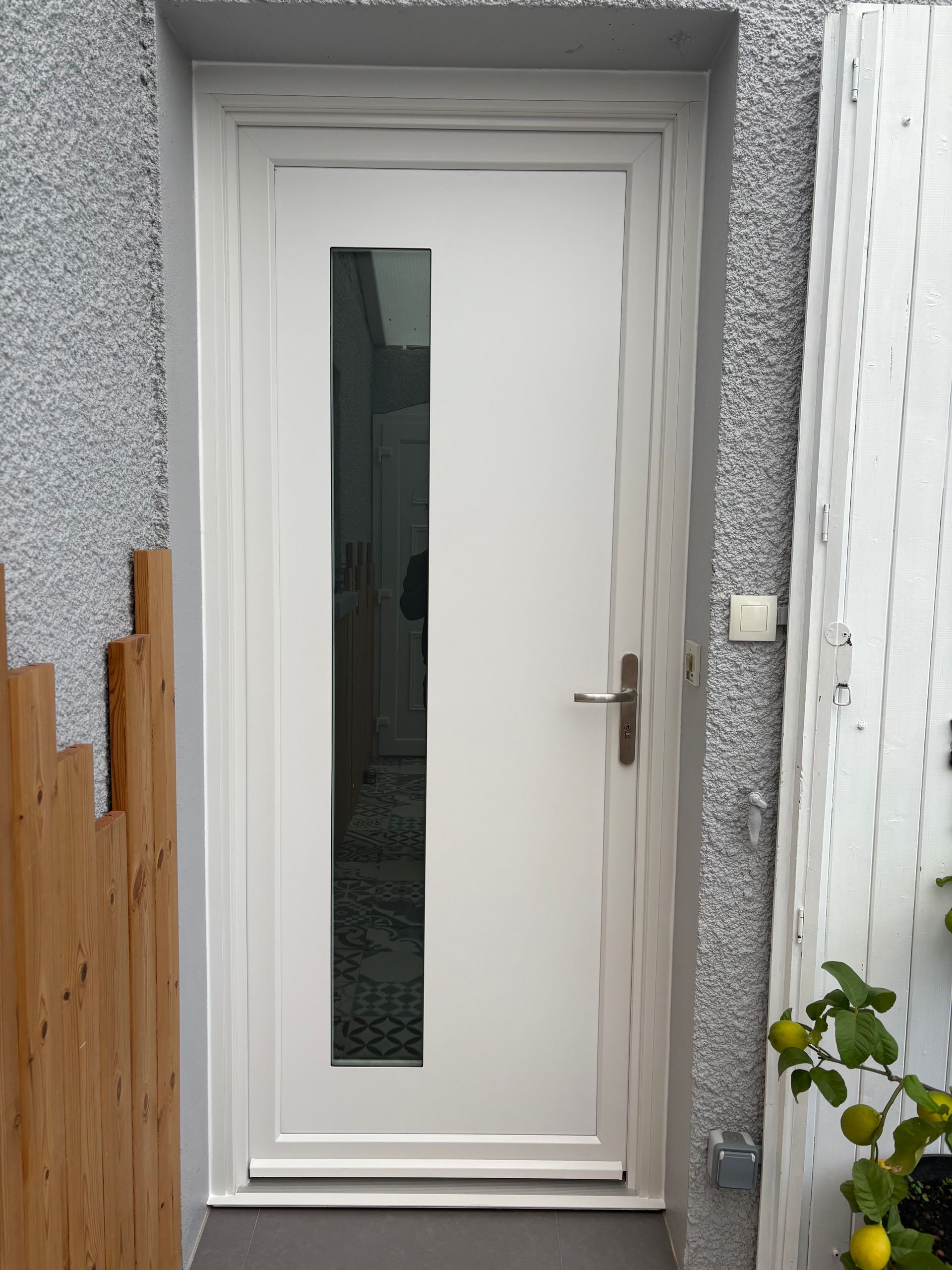 Porte d'entrée blanche avec un étroit panneau de verre dépoli dans un hall d'entrée en stuc gris.