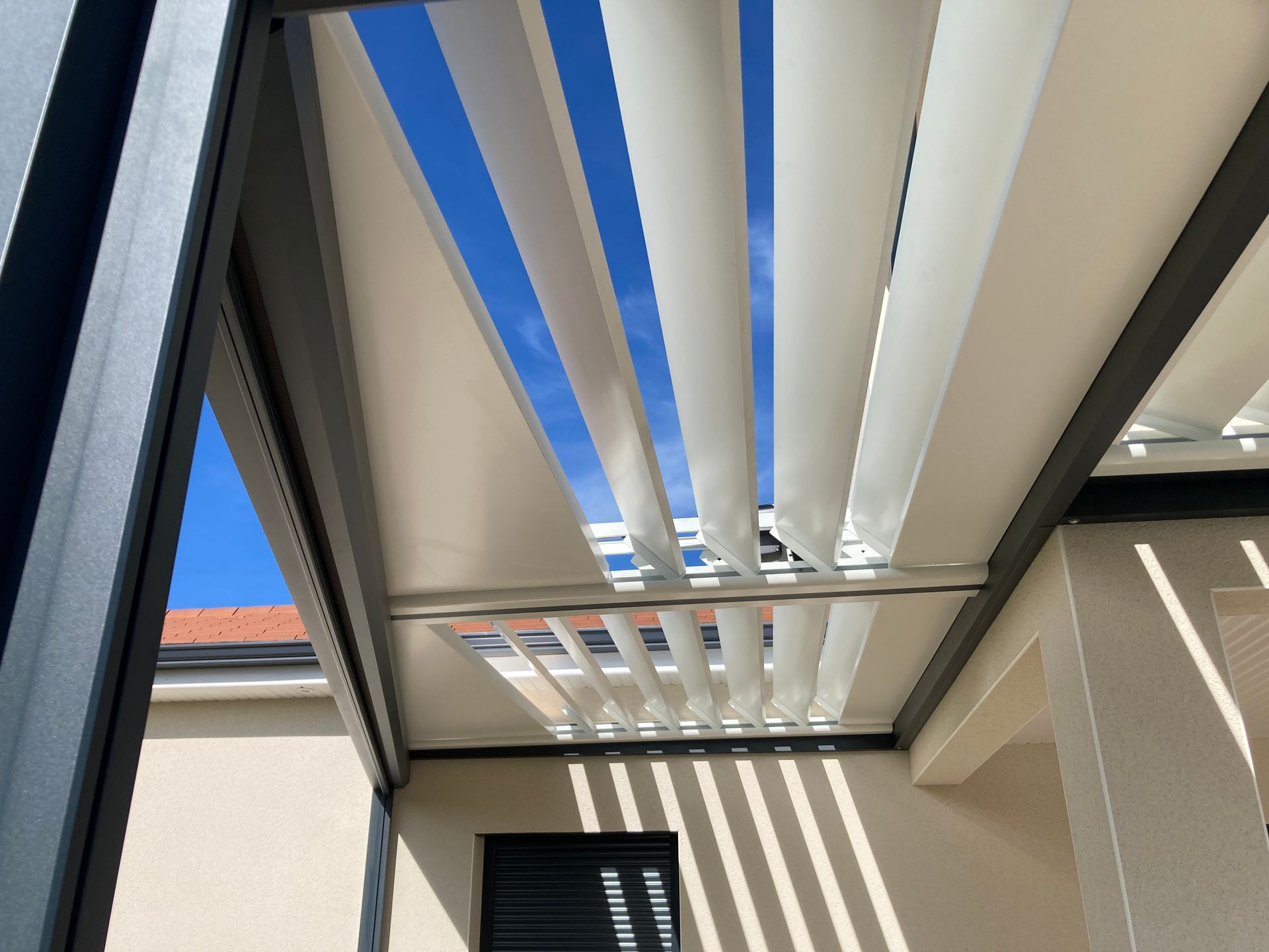 Vue vers le ciel bleu éclatant à travers les lattes blanches ajourées d'un toit de patio moderne à persiennes.