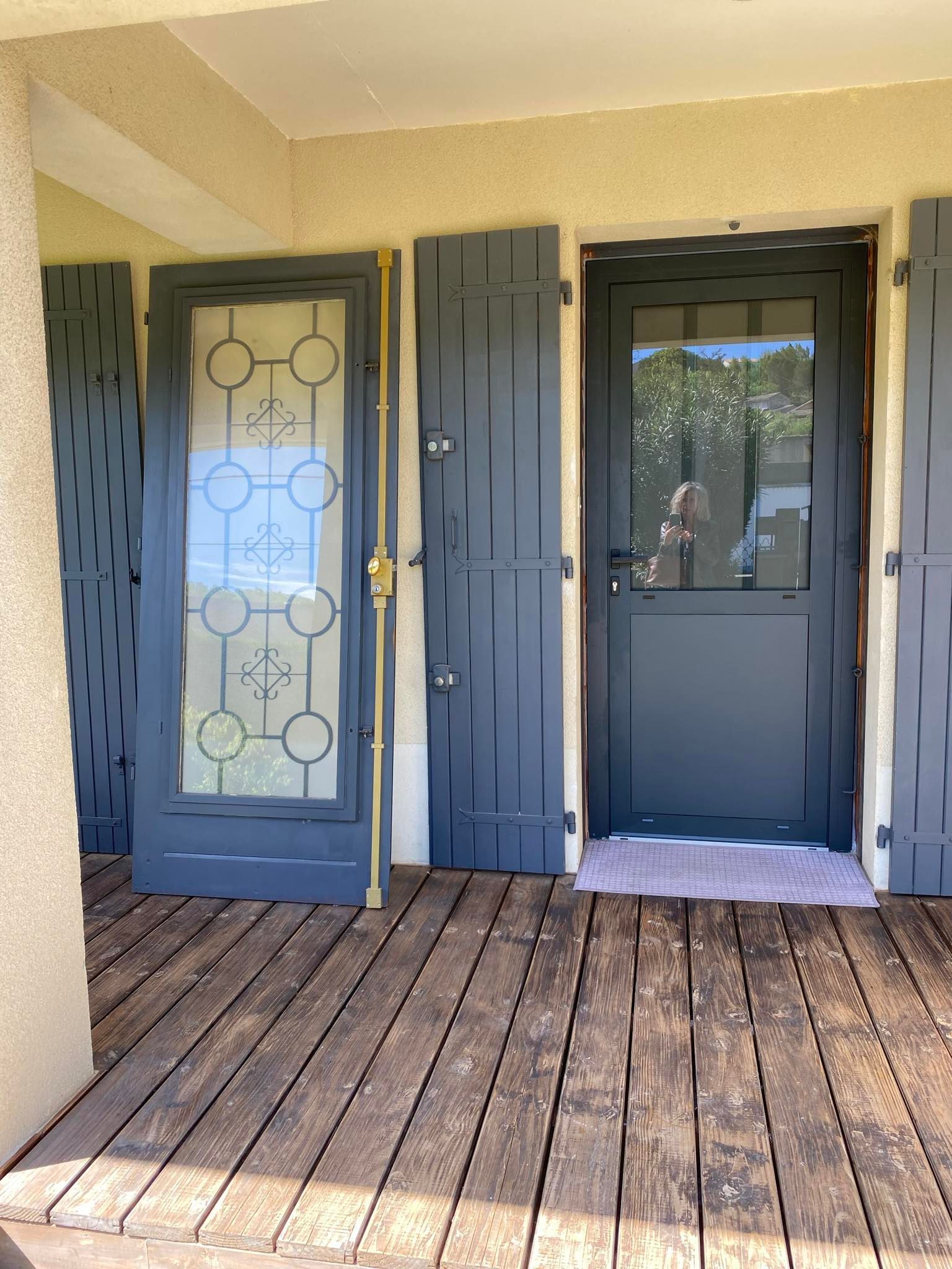 Deux portes gris foncé s'ouvrent sur une terrasse en bois. La porte de gauche est vitrée avec des motifs ; celle de droite est en verre clair.