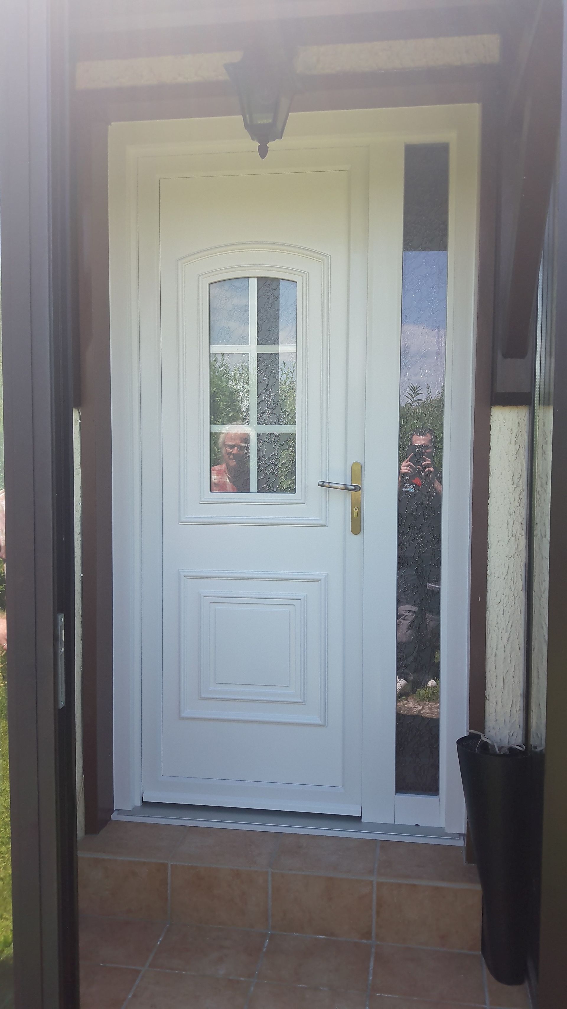 Une porte d'entrée blanche avec une fenêtre en verre et une imposte latérale verticale adjacente, encadrée par des marches carrelées.