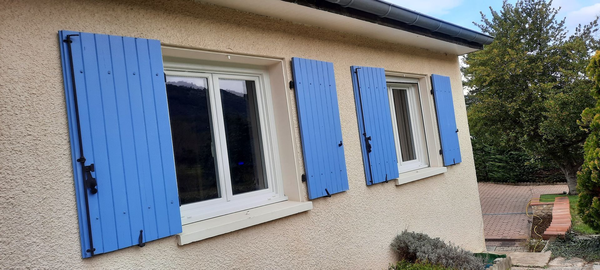 Mur extérieur en stuc clair avec deux fenêtres dotées de volets en bois bleu vif ouverts.