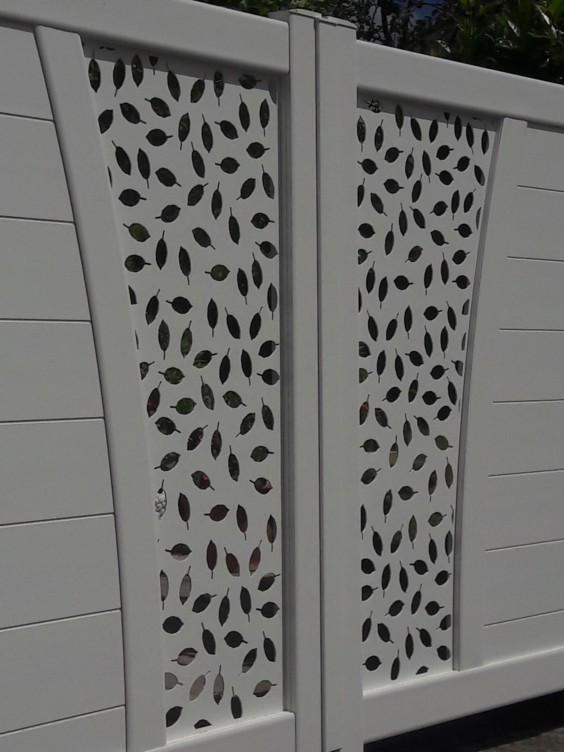 Un portail de clôture blanc orné de deux panneaux décoratifs verticaux à motif de feuilles découpées en noir et blanc.