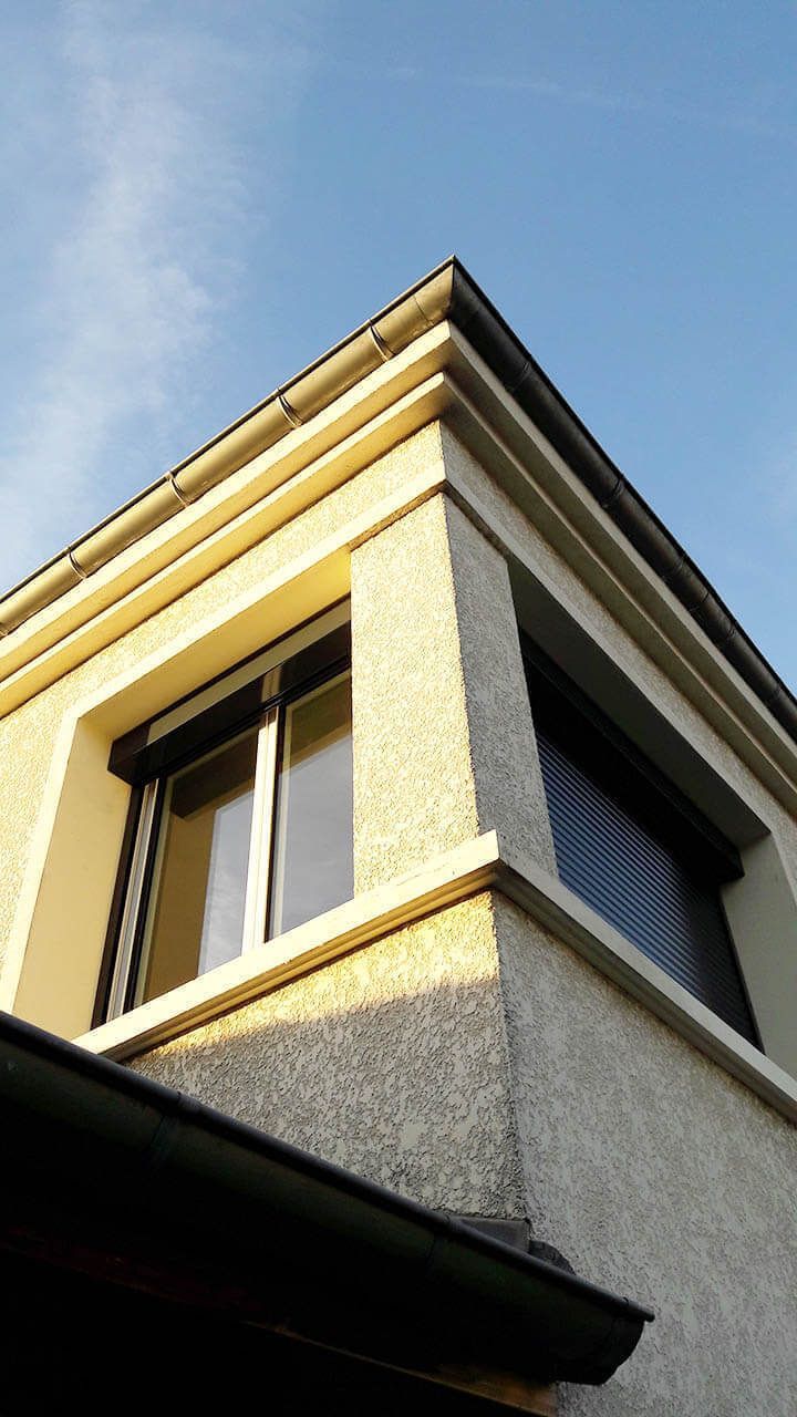 Vue en contre-plongée du coin d'un bâtiment couleur crème présentant des murs en stuc texturé, des moulures décoratives et des fenêtres.