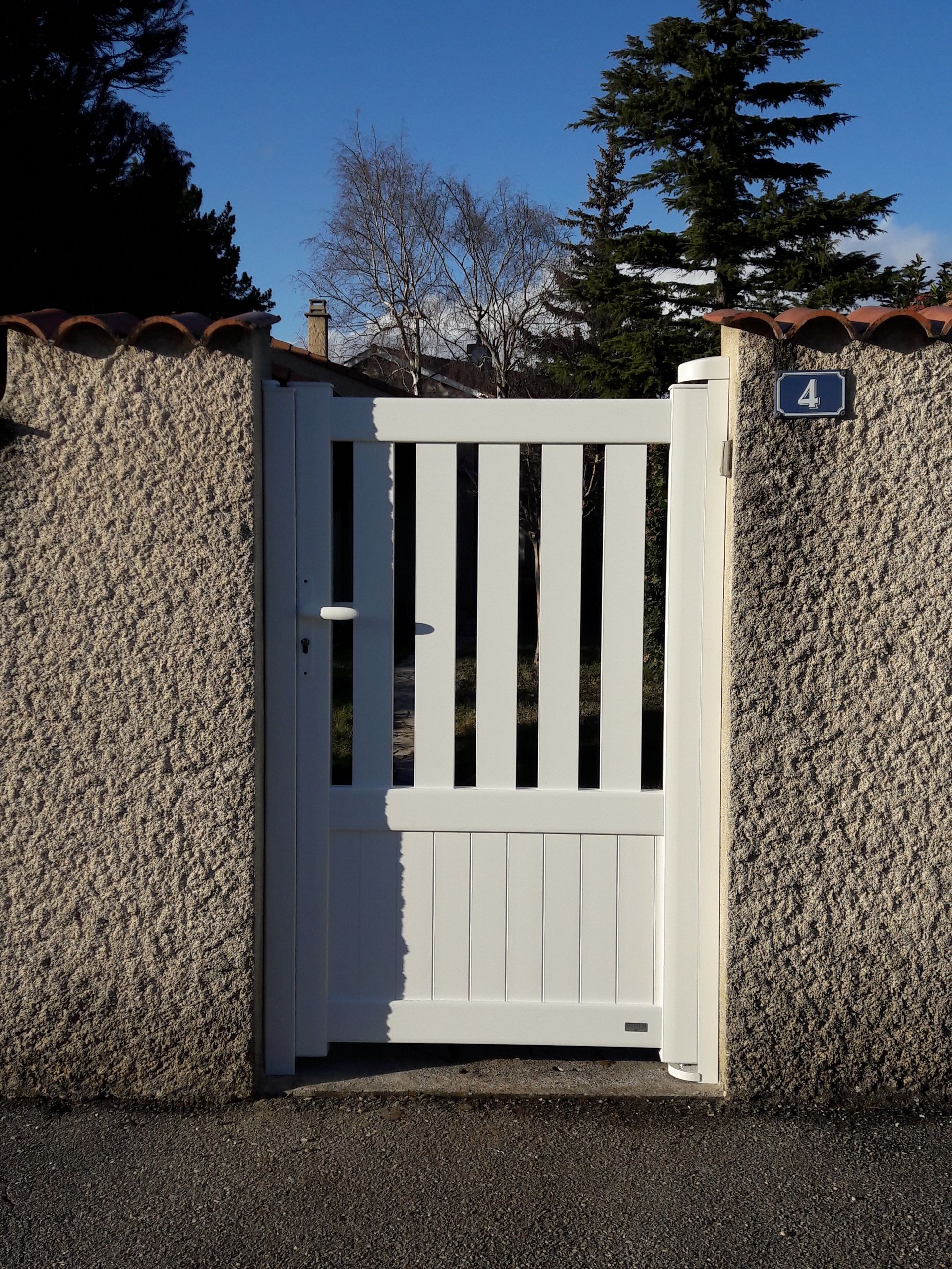 Un portillon blanc, encadré par deux murs en pierre crépie, avec le numéro 4 sur le pilier de droite.