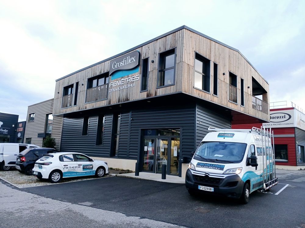 Bâtiment commercial de deux étages avec bardage en bois et une camionnette blanche de l'entreprise garée devant.