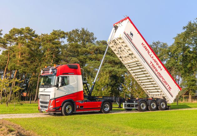 Ein LKW fährt auf einer unbefestigten Straße neben einem Traktor her.