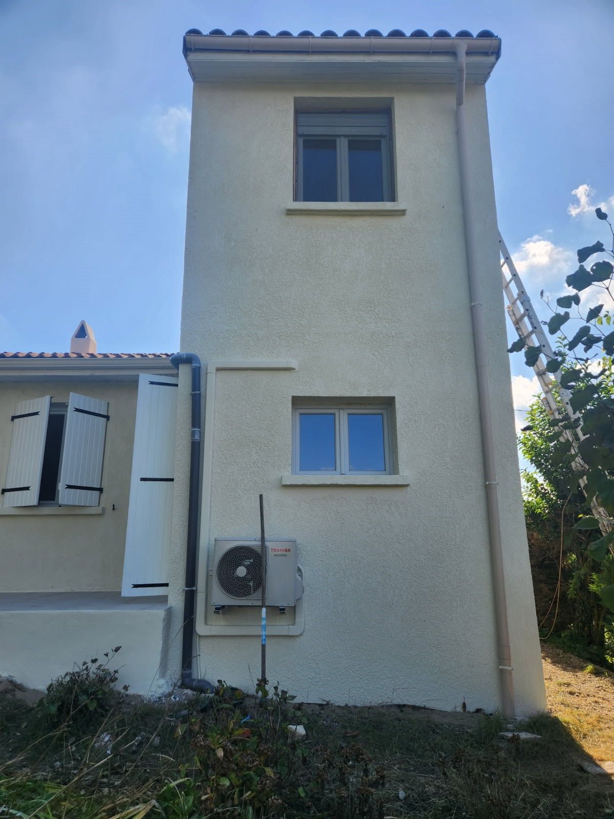 Maison blanche à deux étages avec fenêtres à encadrement bleu et climatiseur mural.