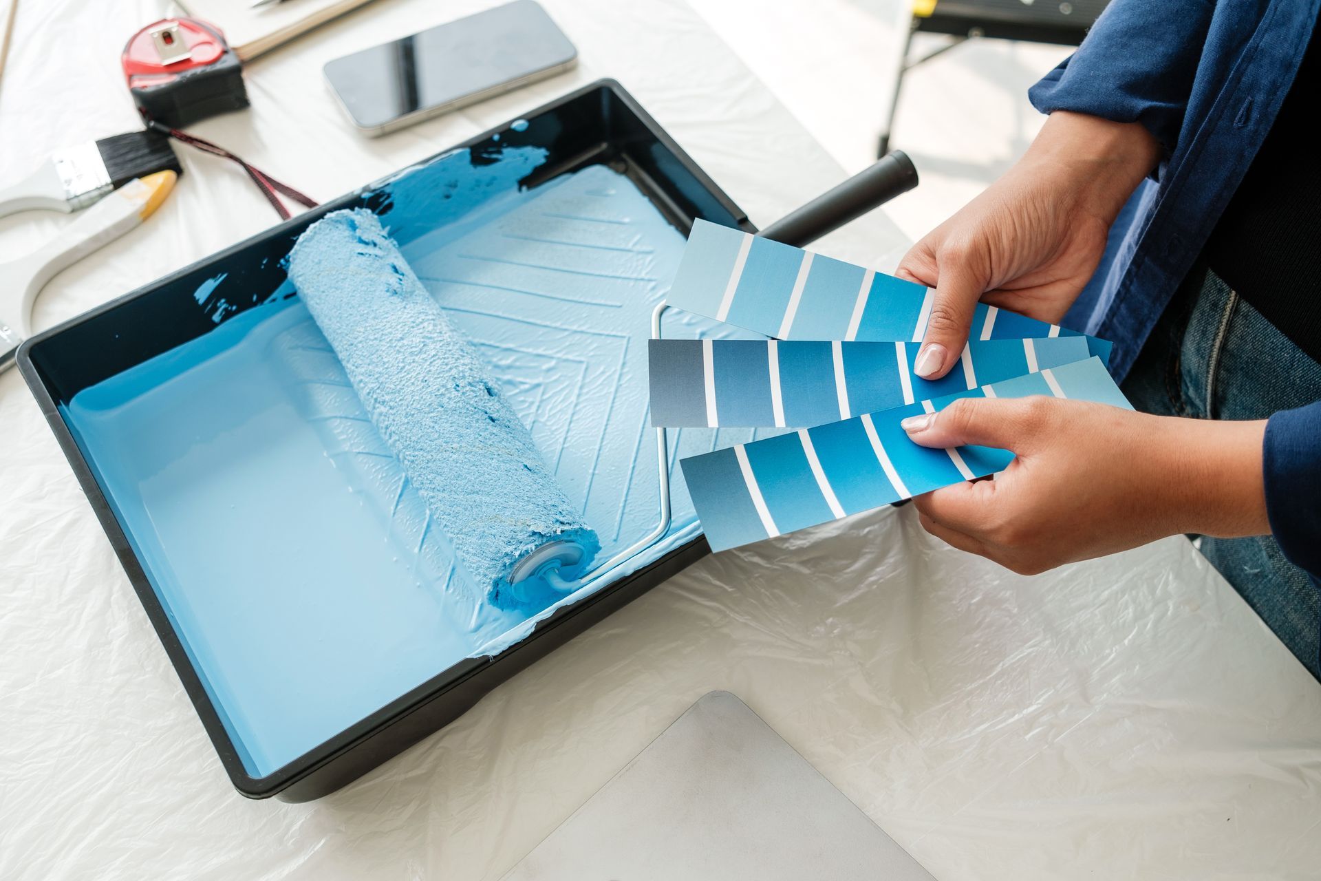 Des mains tenant des échantillons de peinture bleue au-dessus d'un plateau de peinture bleu clair posé sur une table.