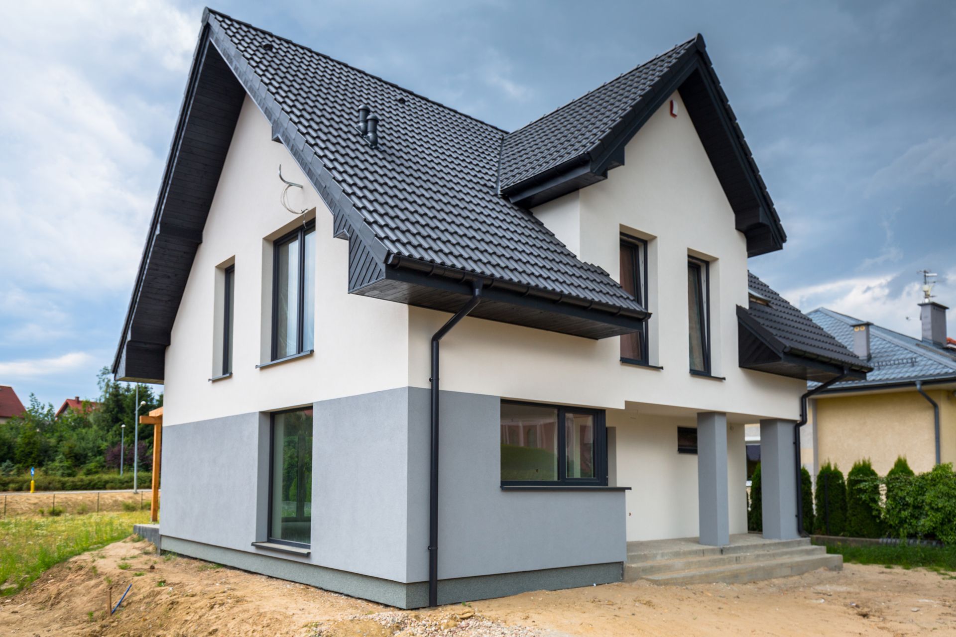 Maison moderne blanche de deux étages avec toit gris foncé et grandes fenêtres sur un terrain gravillonné.