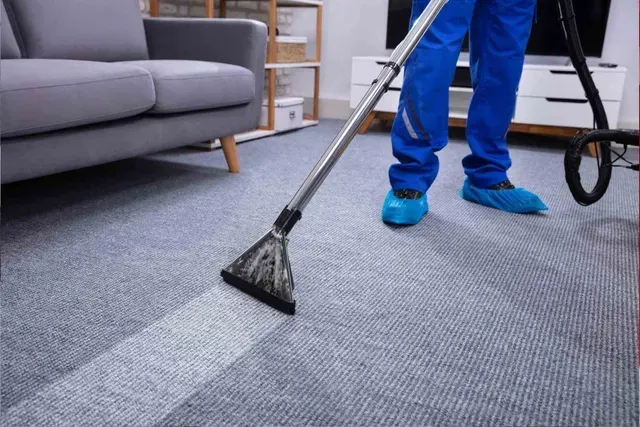 Persona con mono azul aspirando una alfombra, dejando una franja limpia.