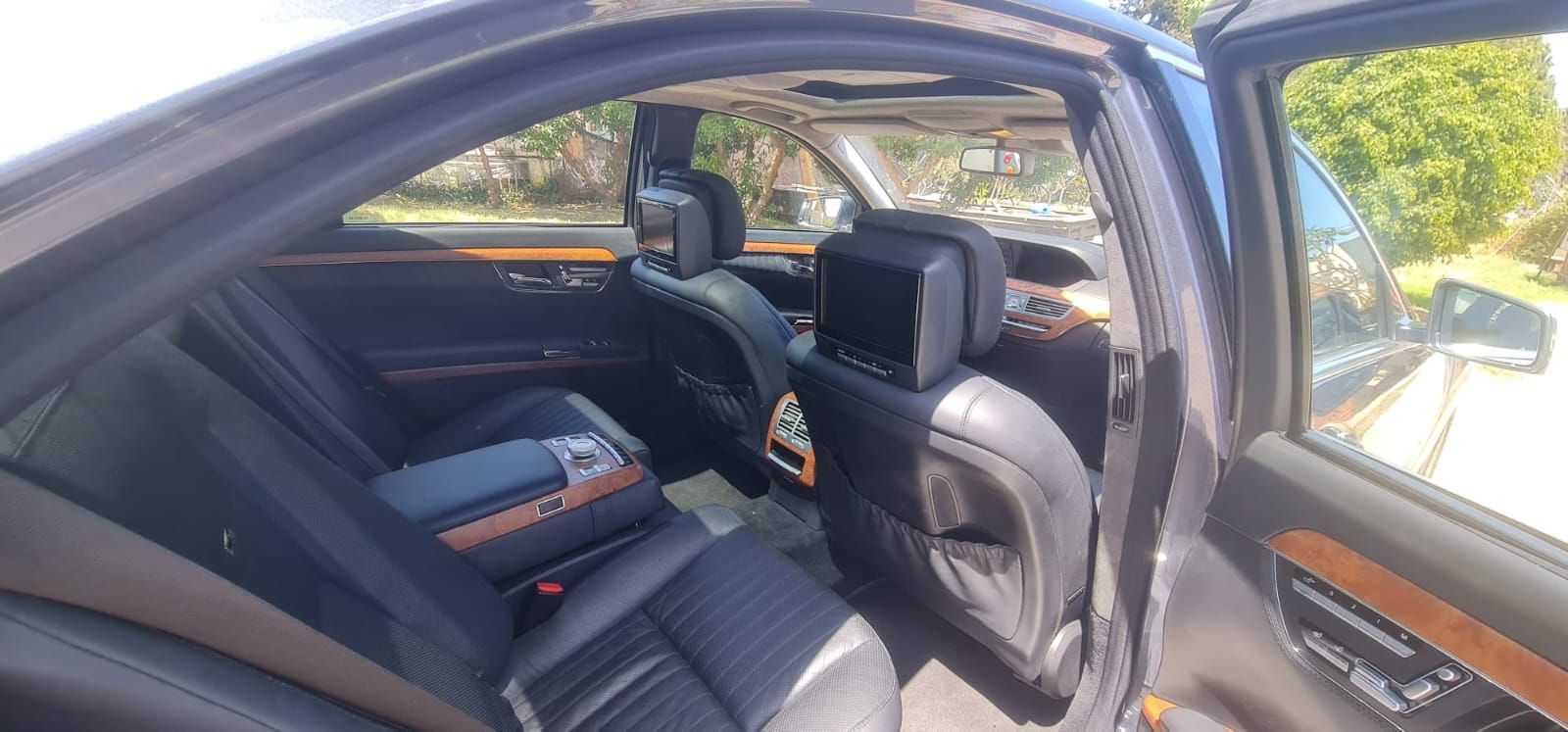 Vista interior de un Mercedes-Benz Clase S sedán negro. Asientos traseros con molduras de madera y pantallas de entretenimiento.