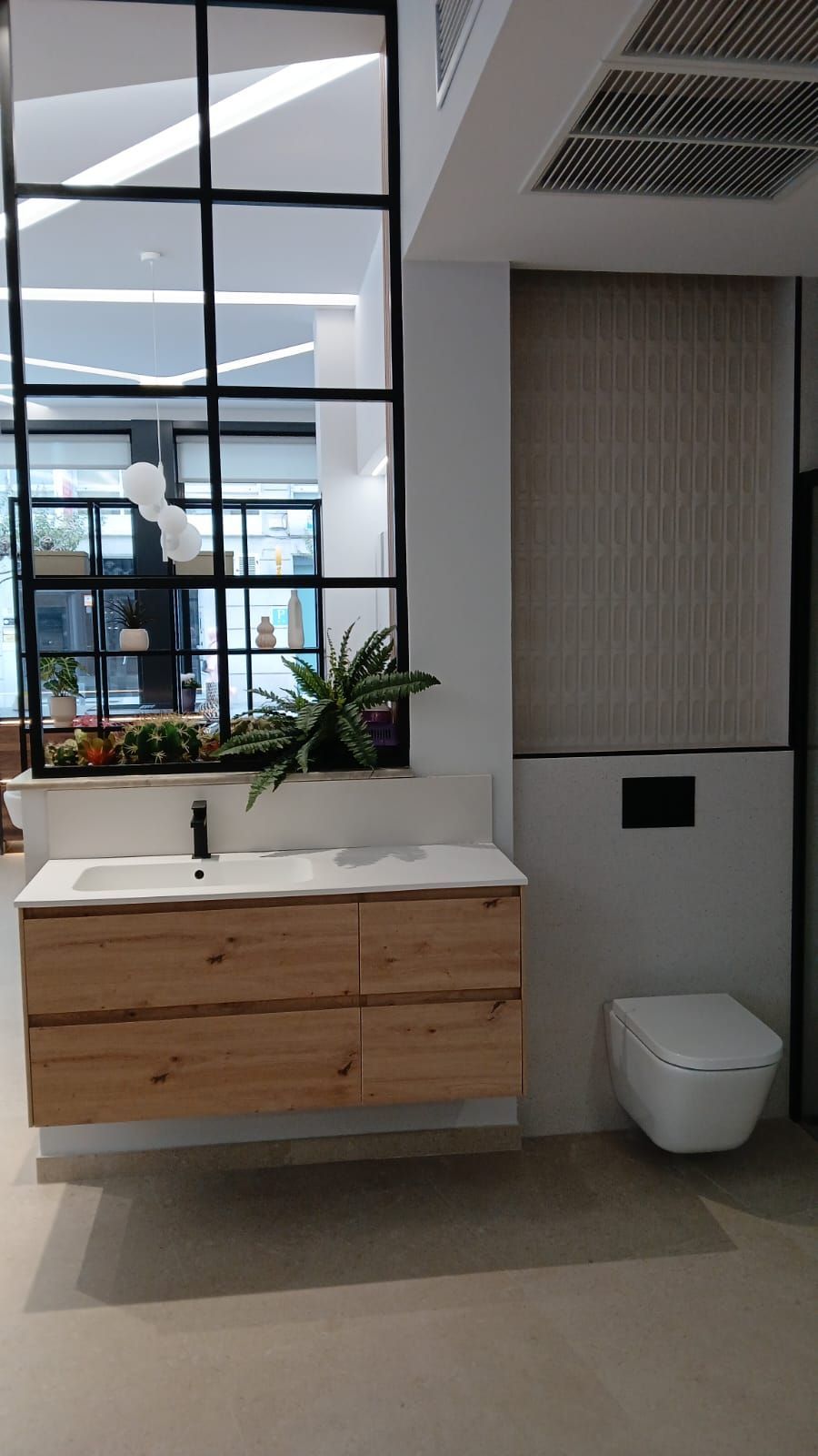 Baño moderno con tocador de madera, espejo con marco negro, inodoro blanco y panel de pared texturizado.