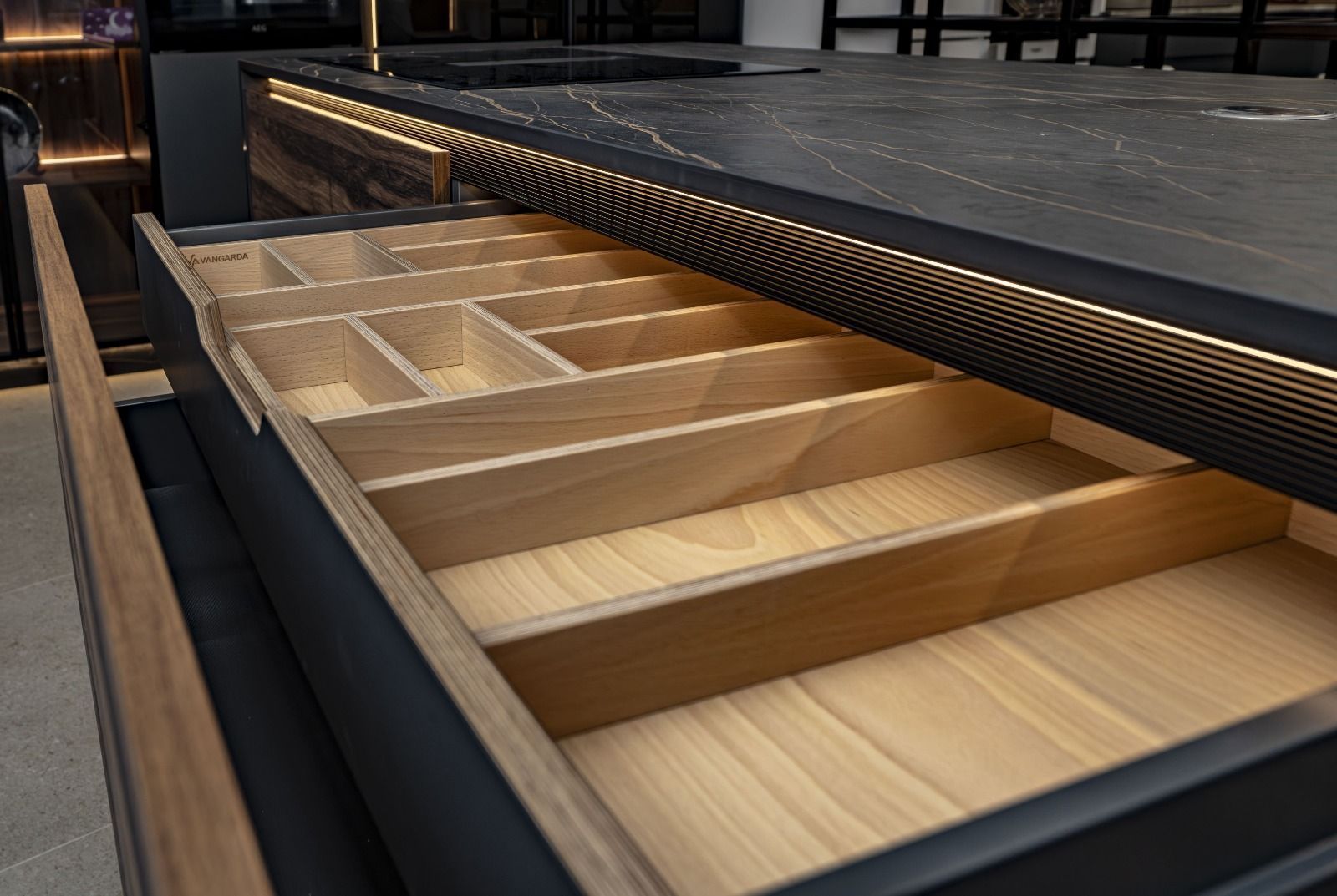 Cajón de cocina de madera abierto con divisores, iluminado por una luz suave.