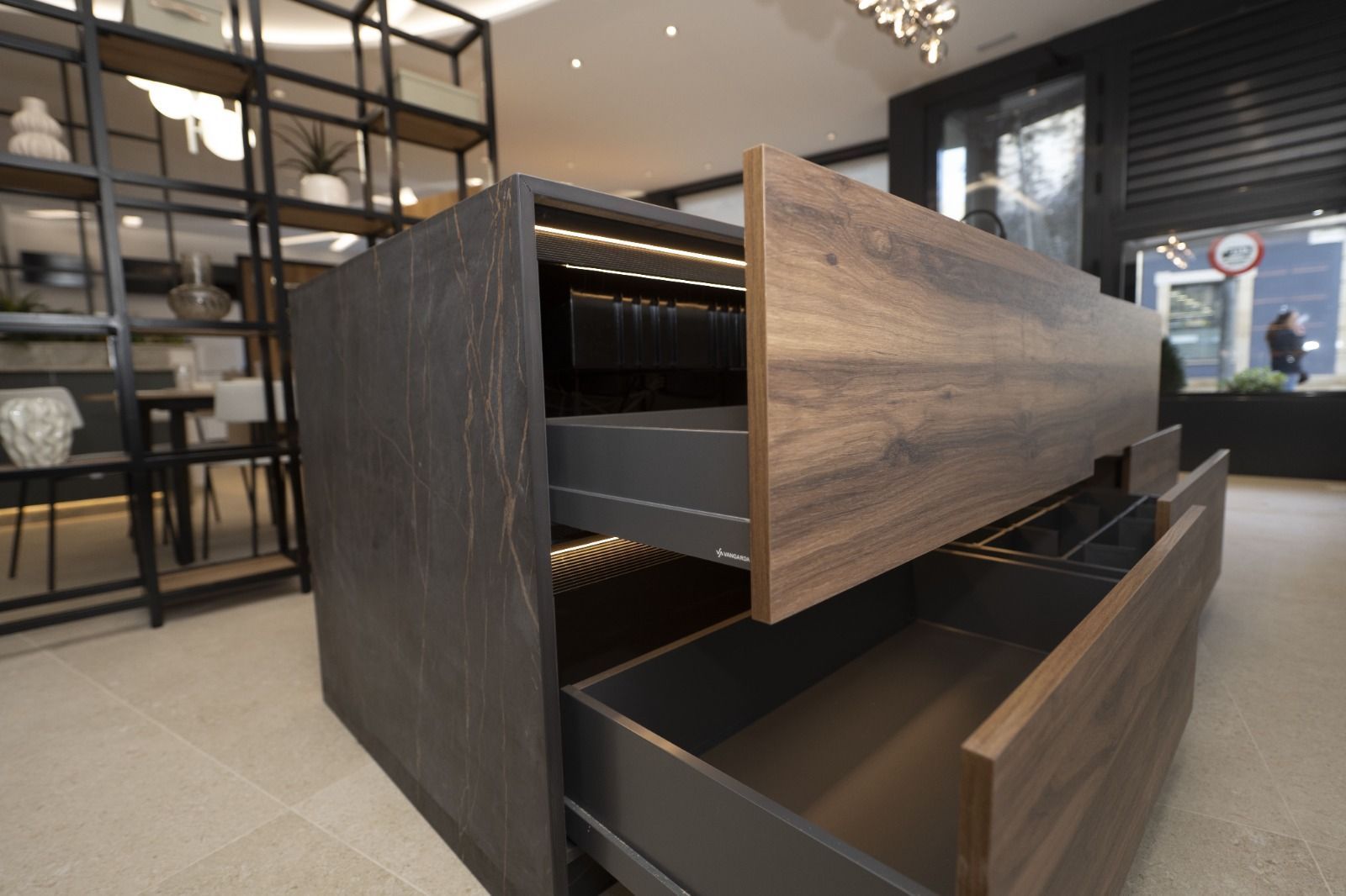 Isla de cocina de madera con cajones abiertos e iluminación integrada. Diseño moderno con estanterías al fondo.