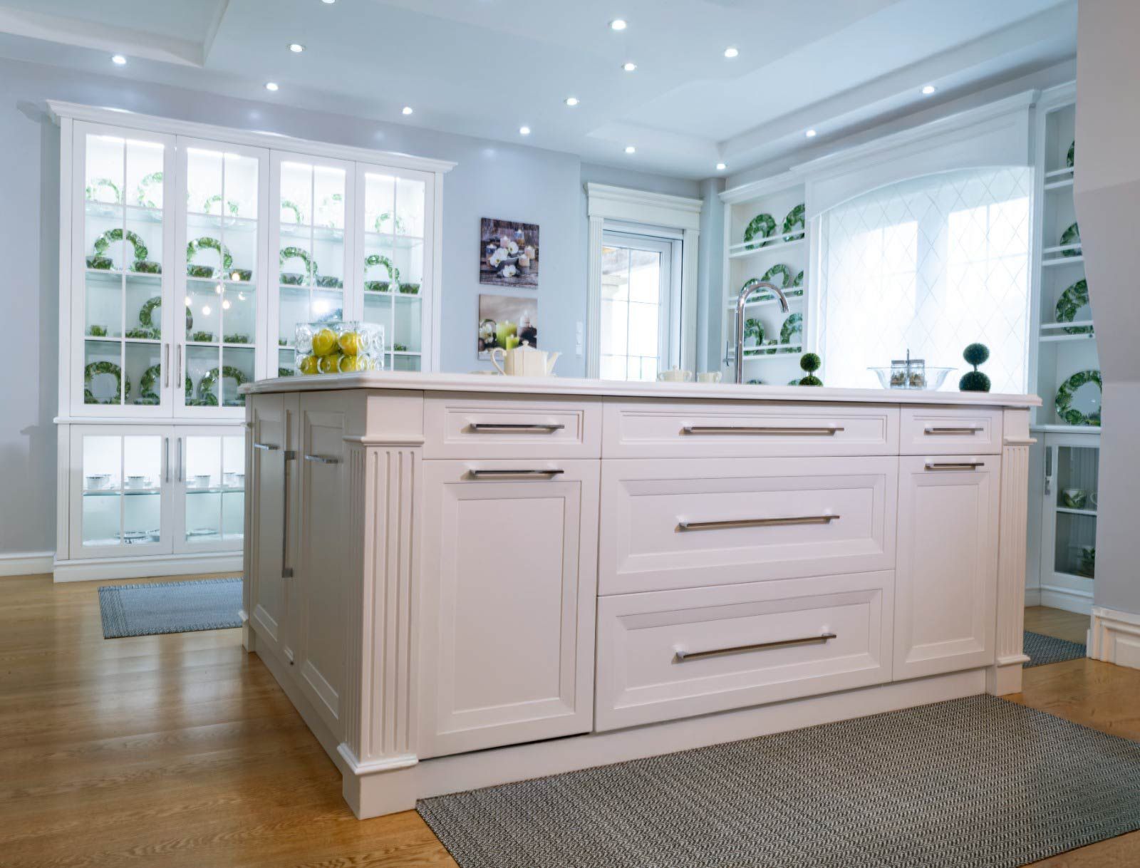 Cocina blanca con isla, gabinetes con frente de vidrio y una pared azul claro.