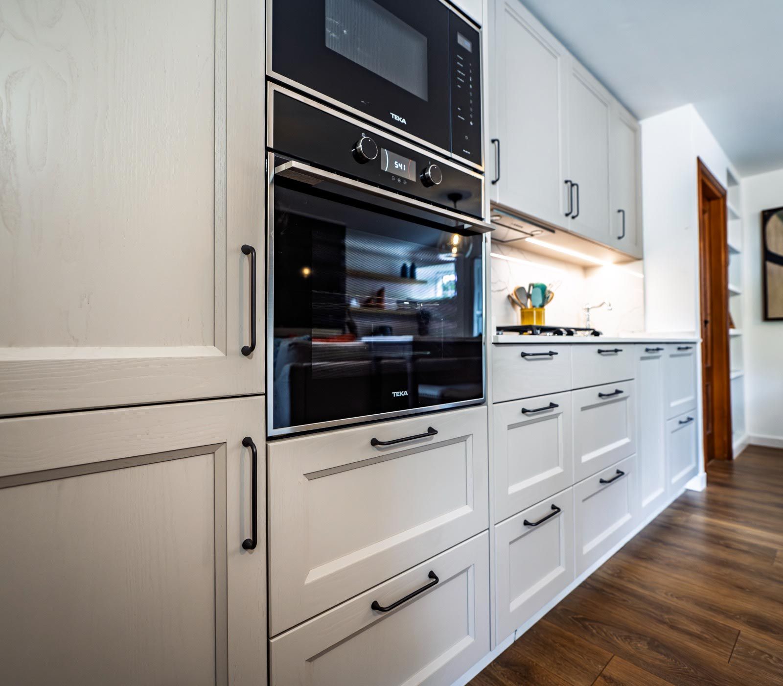 Gabinetes de cocina blancos con electrodomésticos y herrajes negros.
