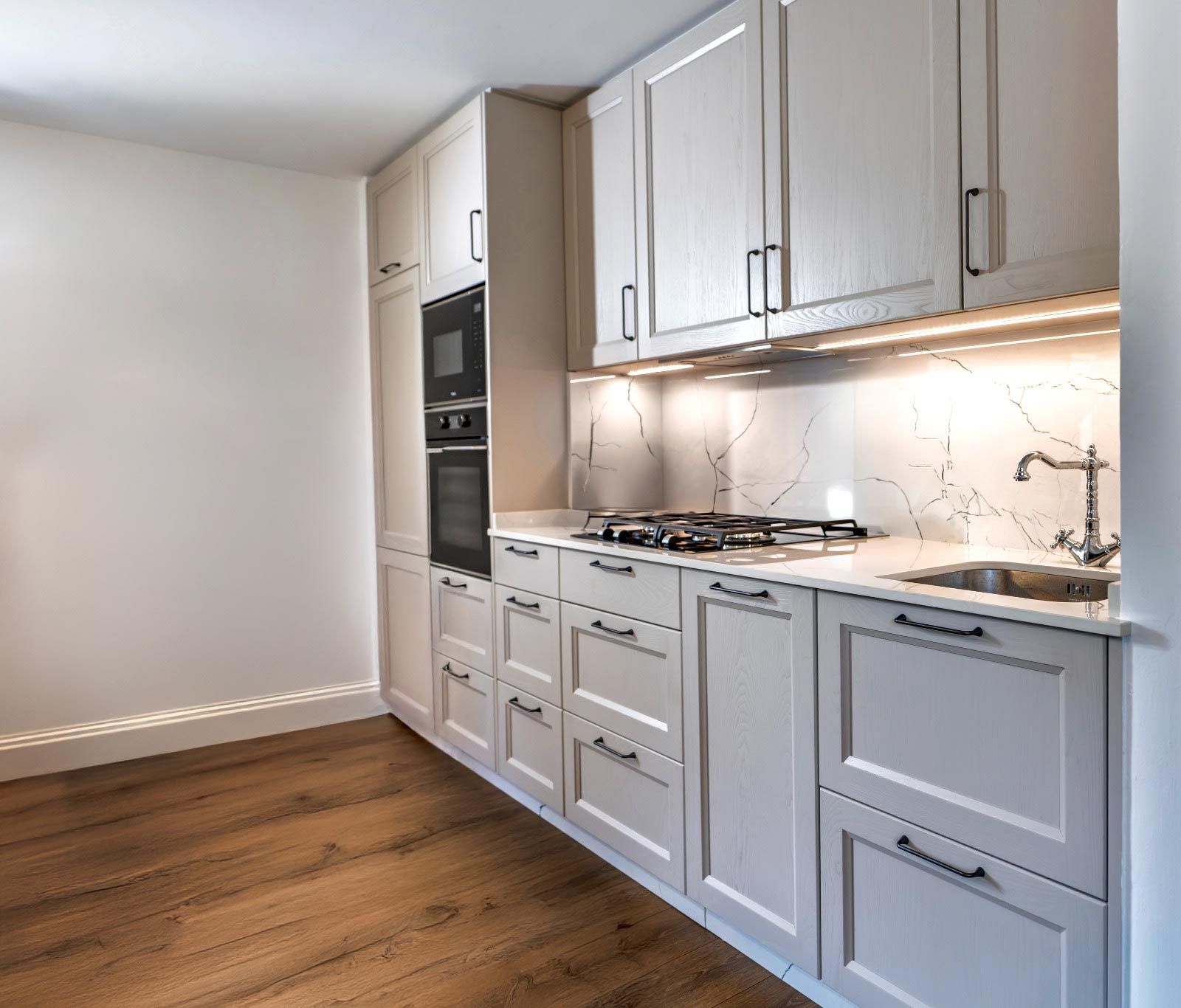 Gabinetes de cocina de color crema con horno y anafe incorporados, encimeras blancas y pisos de madera clara.