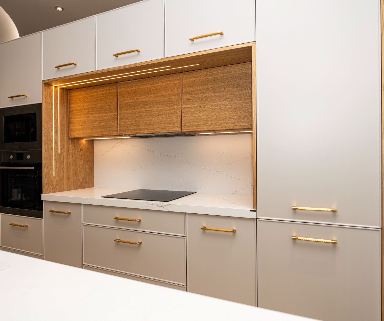 Cocina moderna con gabinetes gris claro, herrajes dorados y detalles de madera.