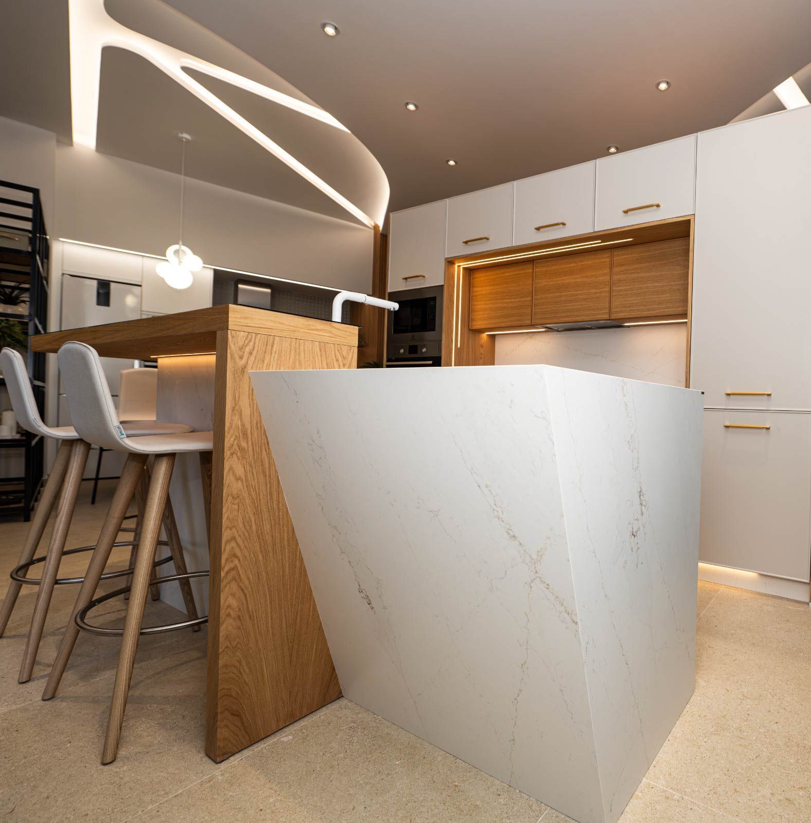 Cocina moderna con encimeras blancas, detalles de madera y taburetes de bar.