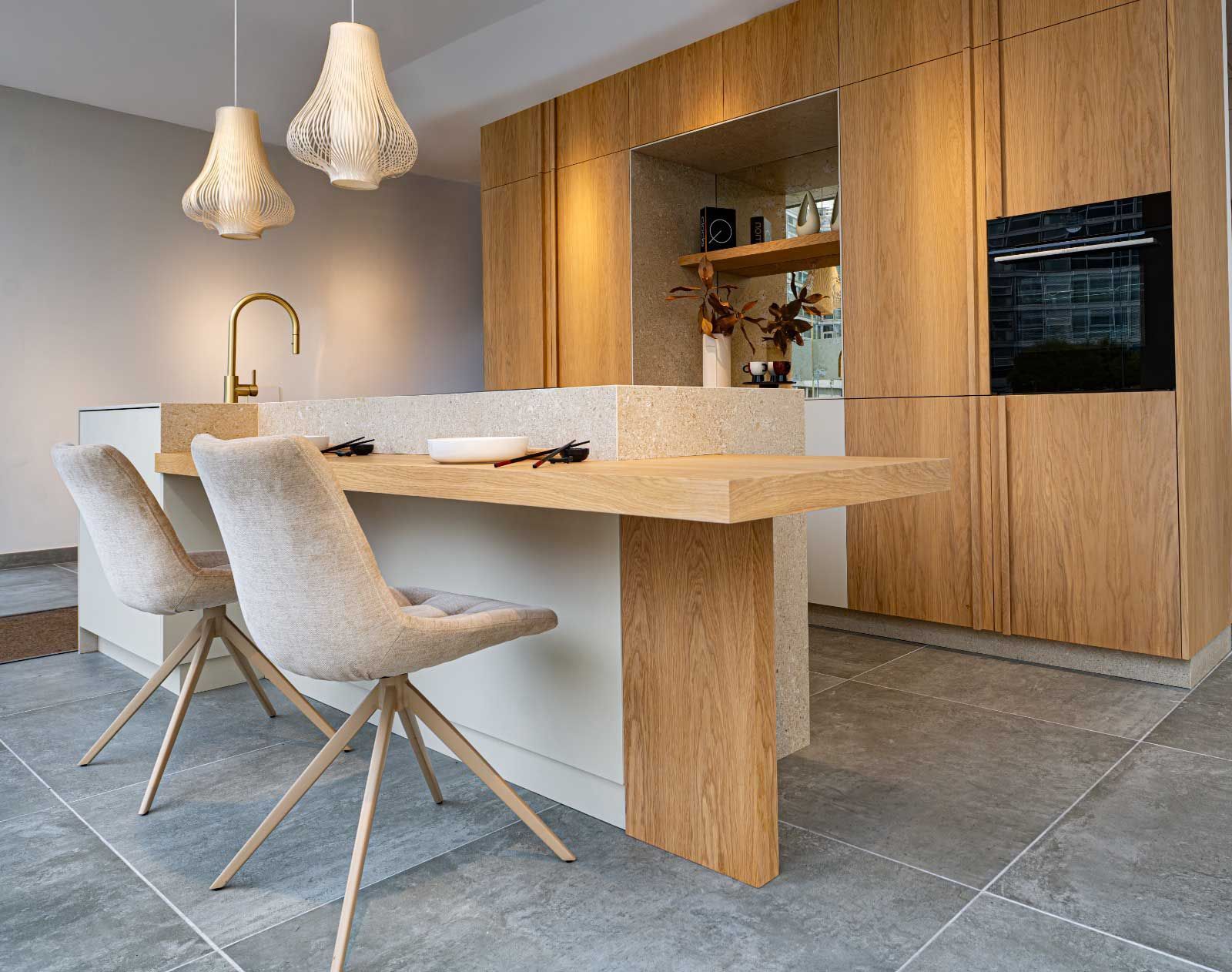 Cocina moderna con gabinetes de madera clara, isla con asientos, horno y luces colgantes.