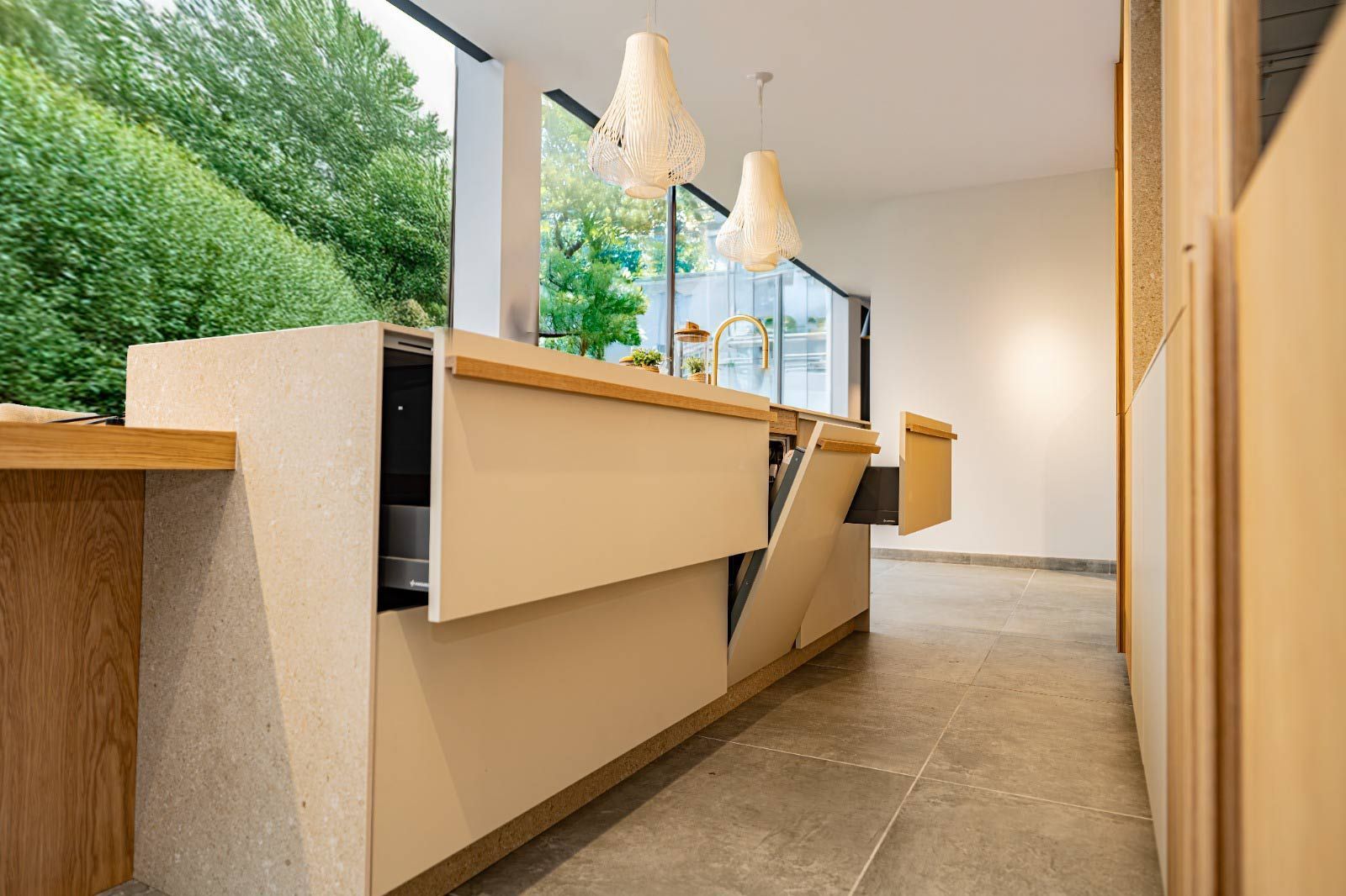 Isla de cocina moderna con cajones abiertos, detalles de madera clara y una gran ventana con vista a la vegetación.
