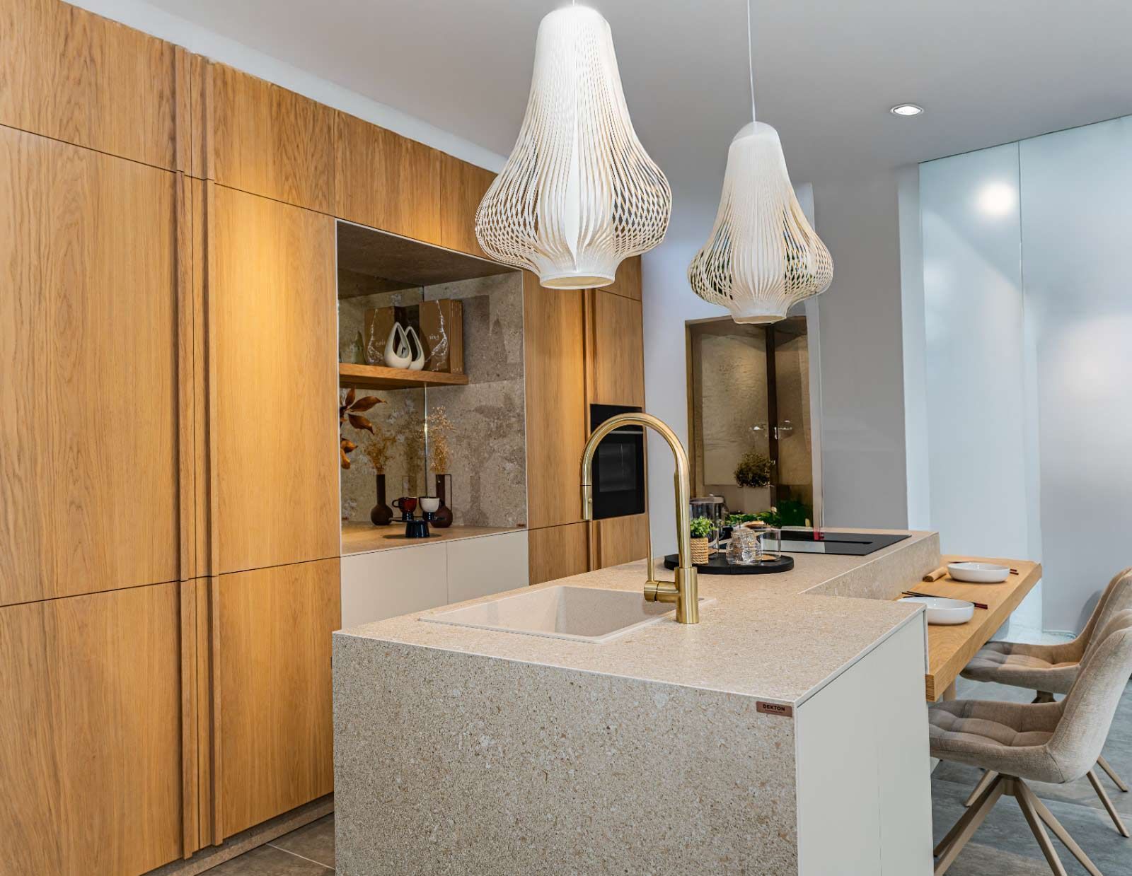 Cocina moderna con gabinetes de madera, isla, grifería dorada, luces colgantes.