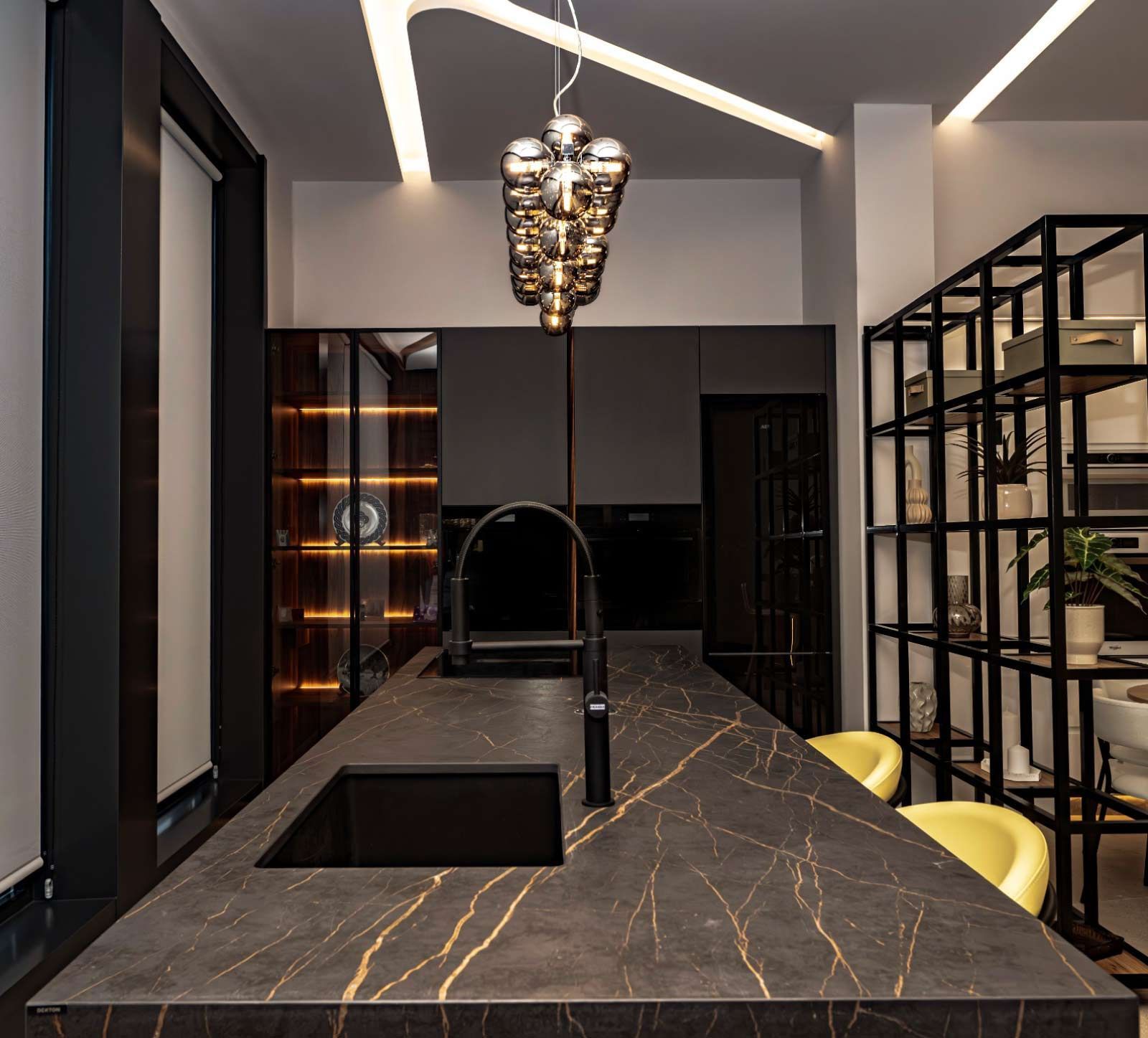 Cocina moderna con encimera oscura, grifo negro, iluminación cenital y estantería.