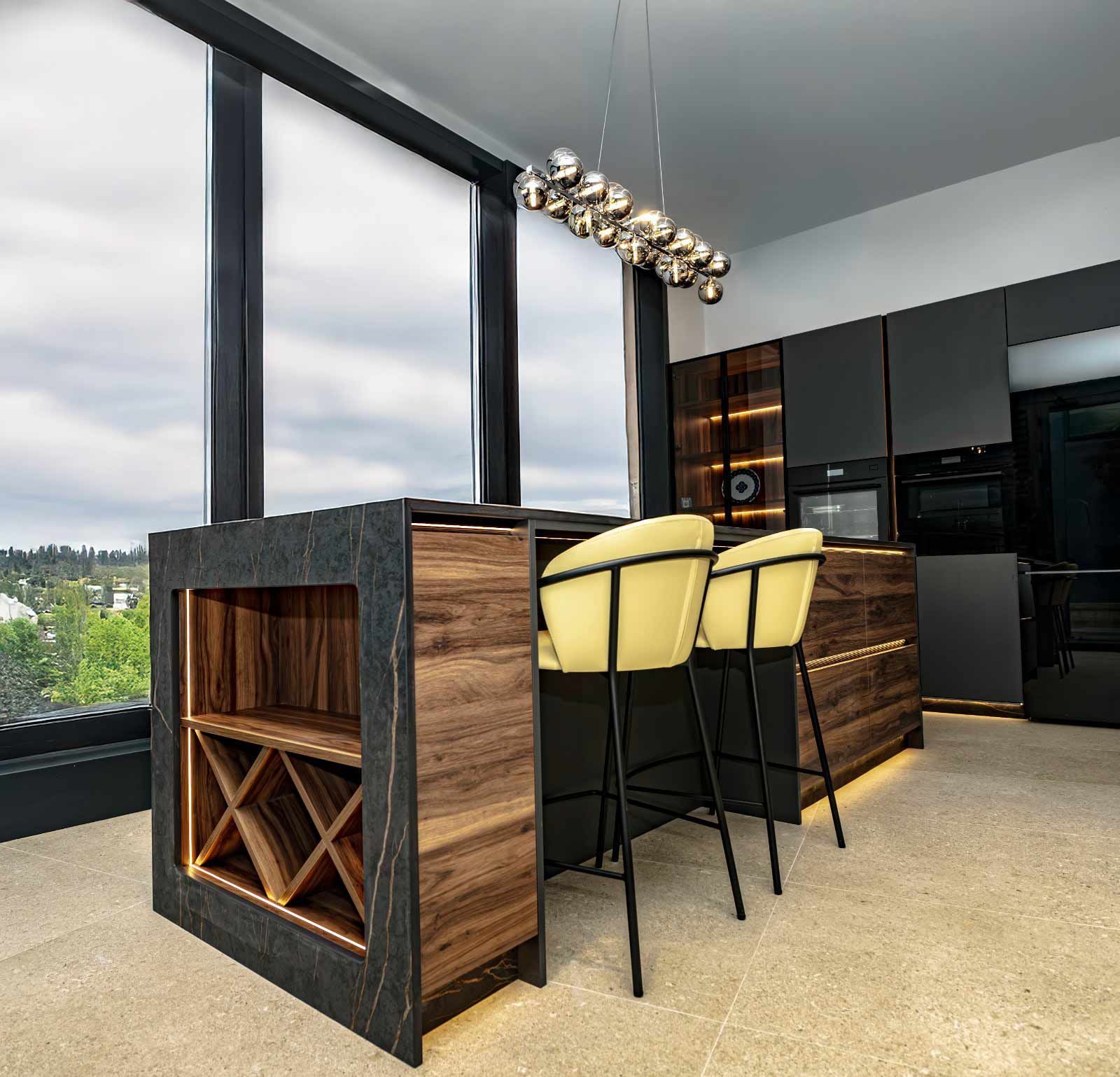 Cocina moderna con isla, botellero, taburetes amarillos y gabinetes oscuros.
