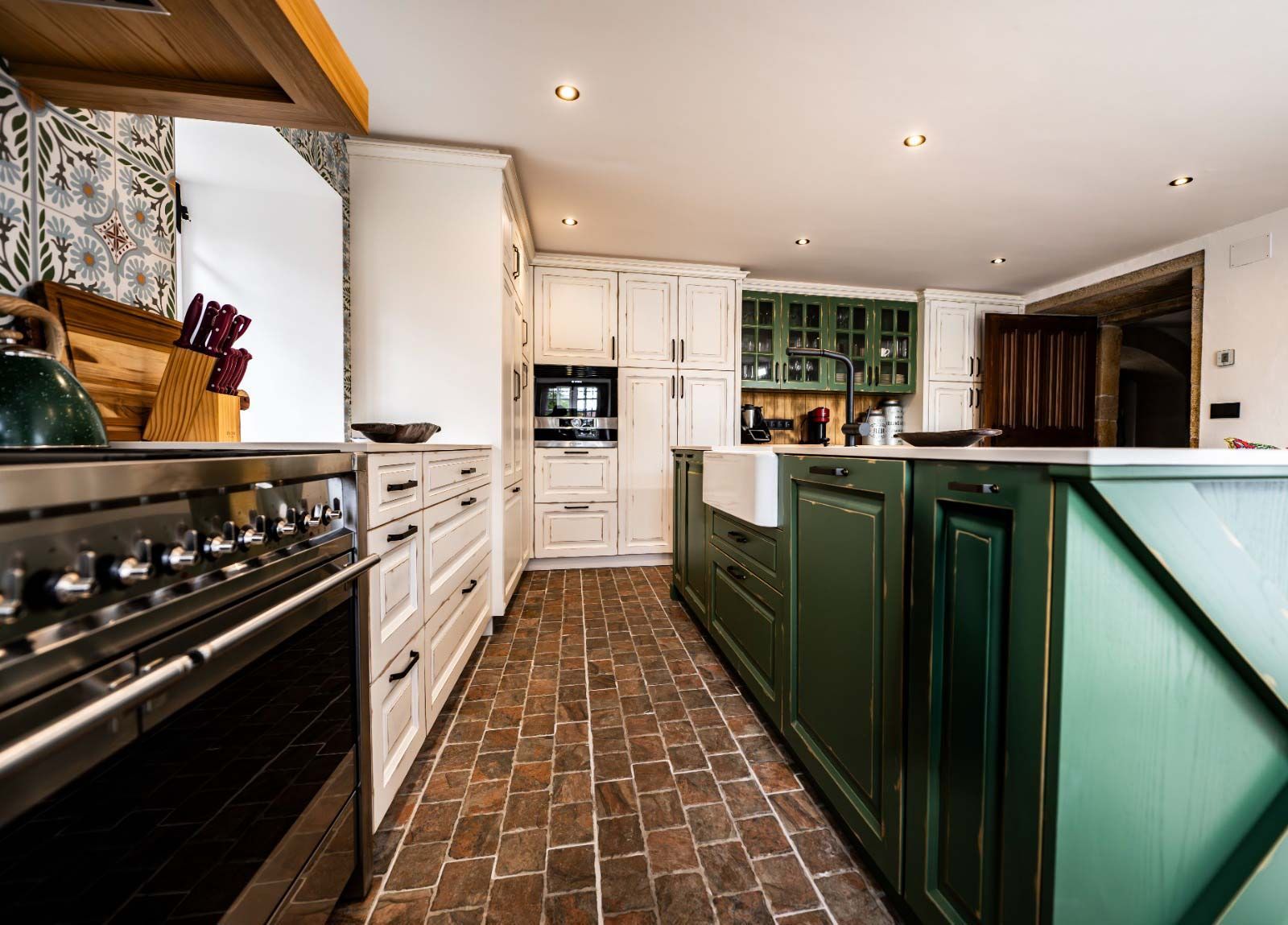 Cocina con gabinetes blancos, isla verde y piso de ladrillo.