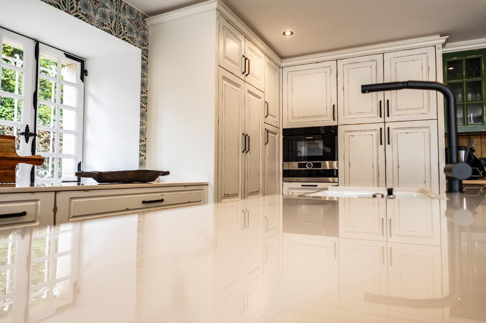 Cocina blanca con encimera brillante, gabinetes, grifo negro y ventana.